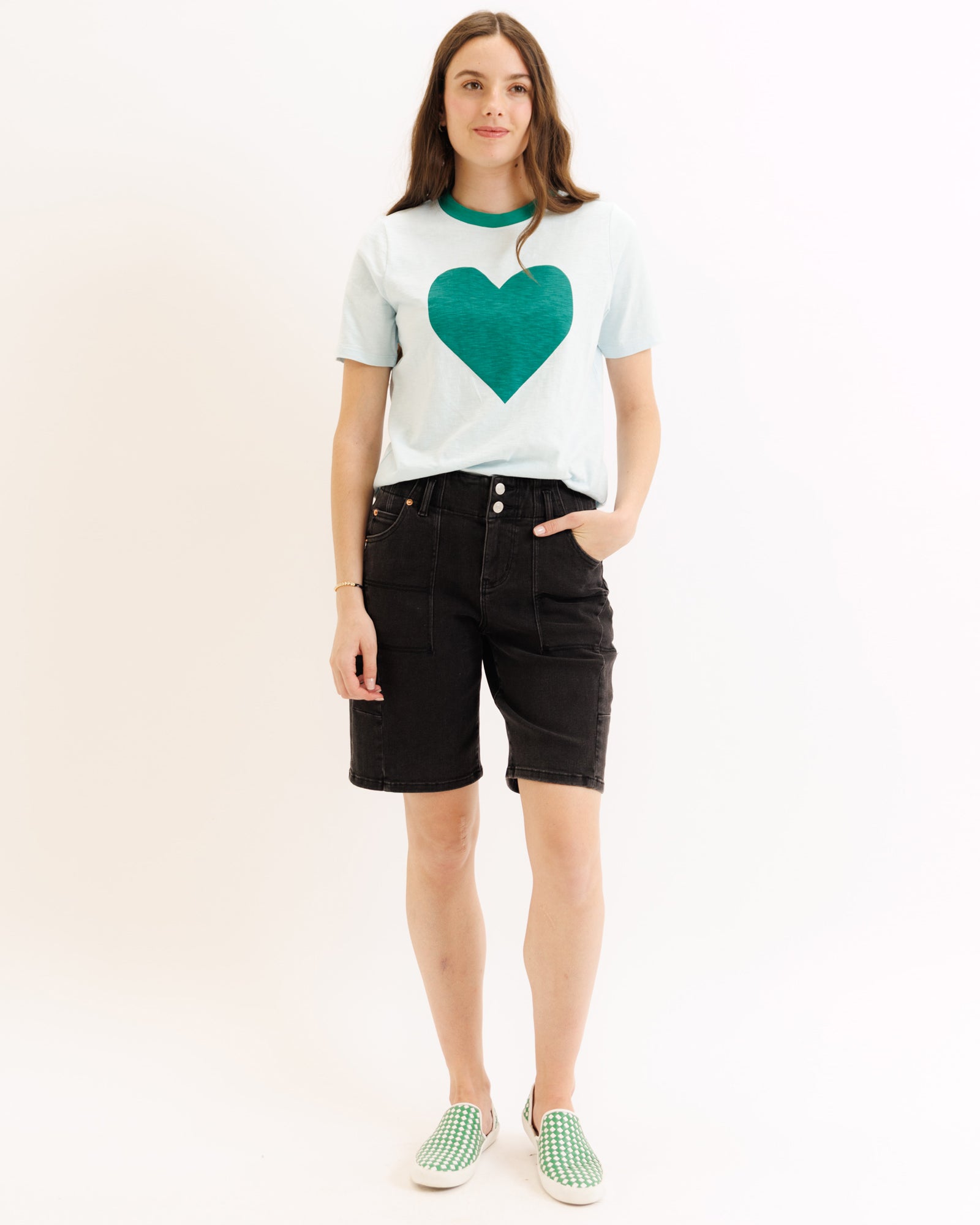 Person wearing a white t-shirt with a green heart design and black shorts on a white background