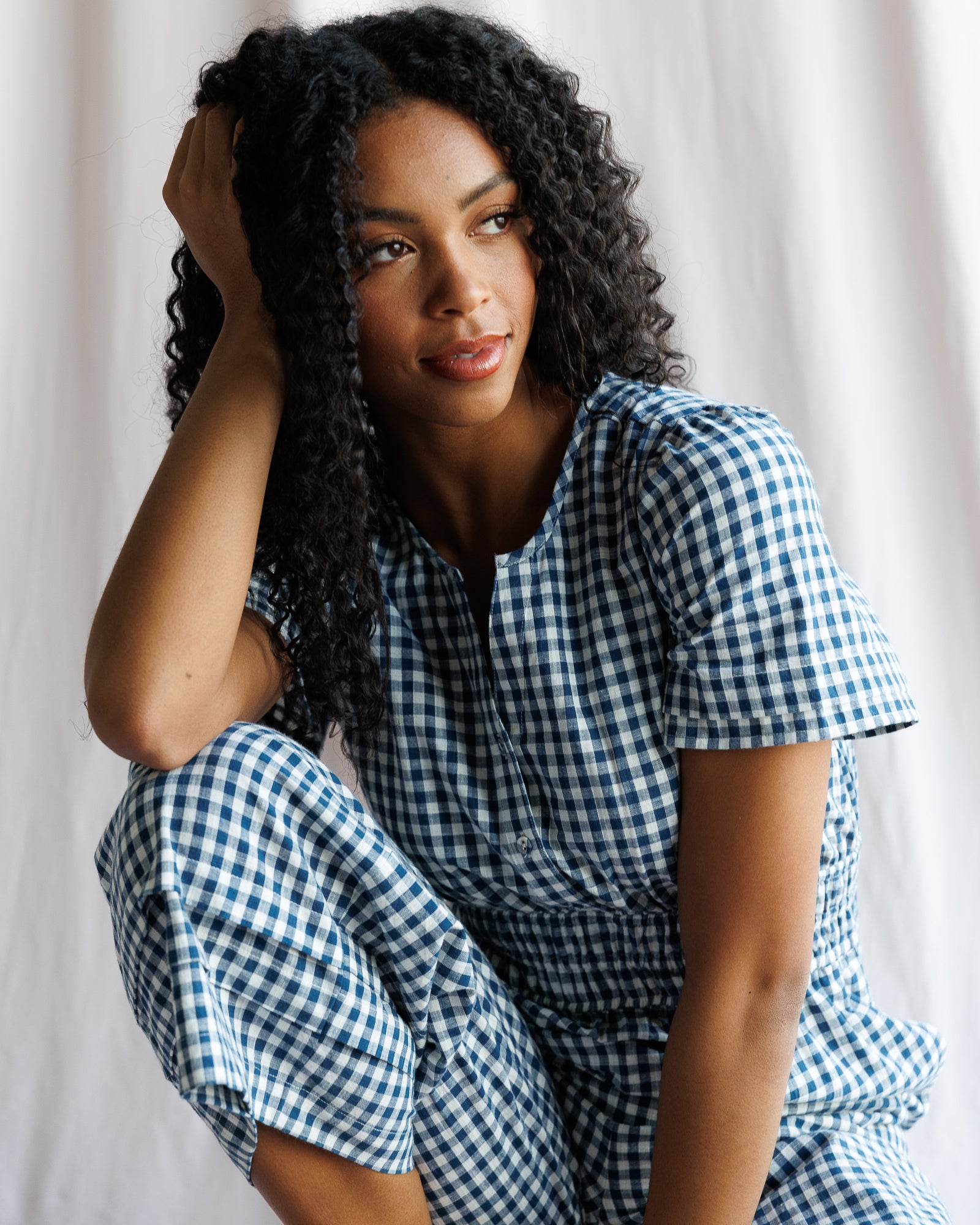 Woman wearing a blue and white checkered outfit sitting against a plain background