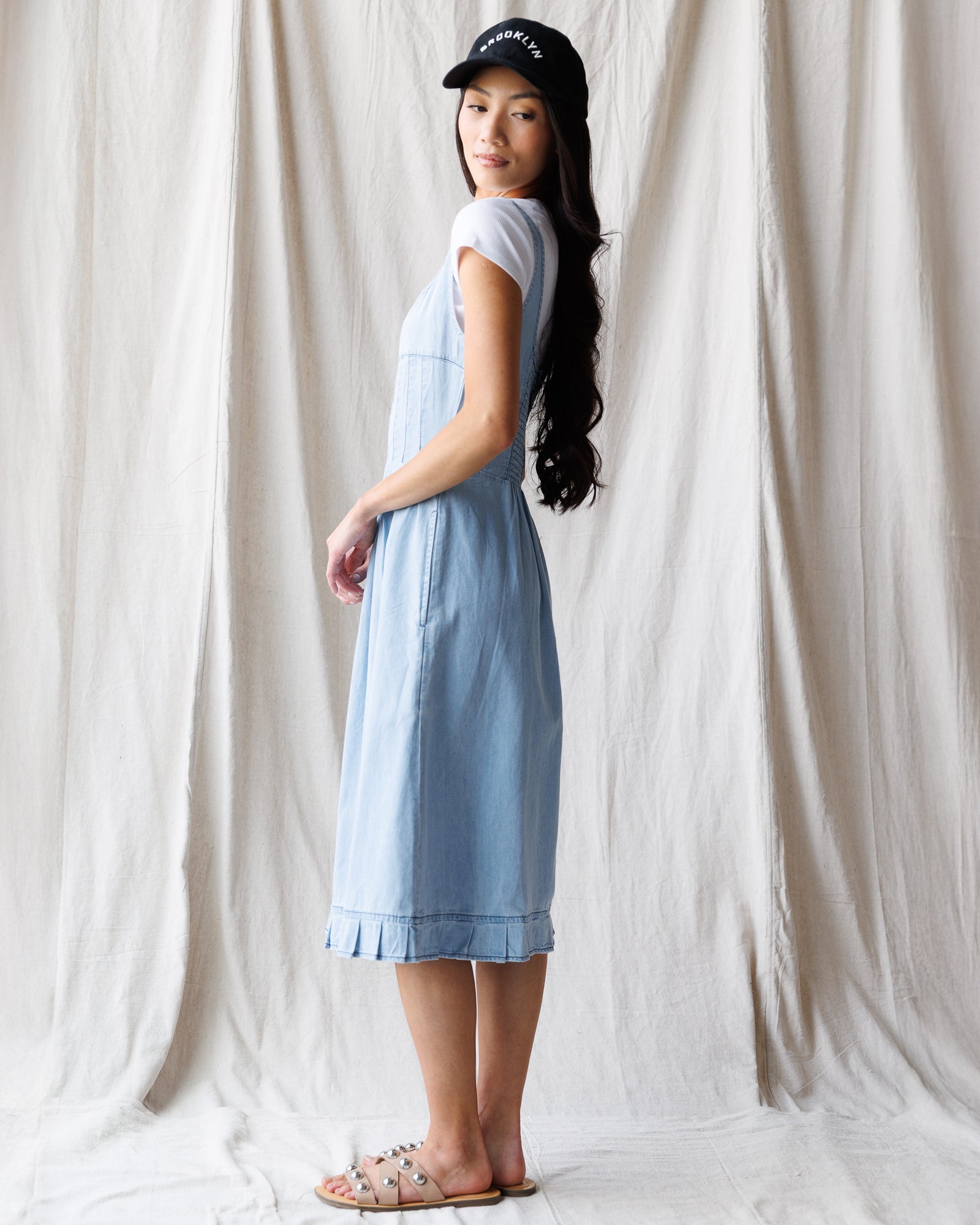 Woman wearing a light blue dress and black cap against a white curtain background