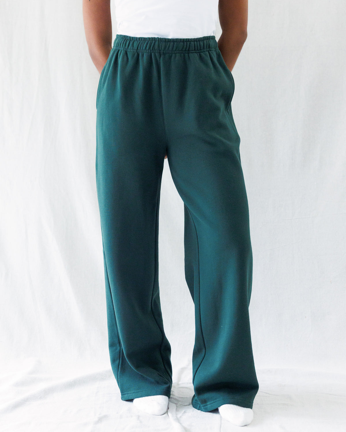 A person wearing dark teal green wide-leg sweatpants, shown from the waist down against a white fabric backdrop.