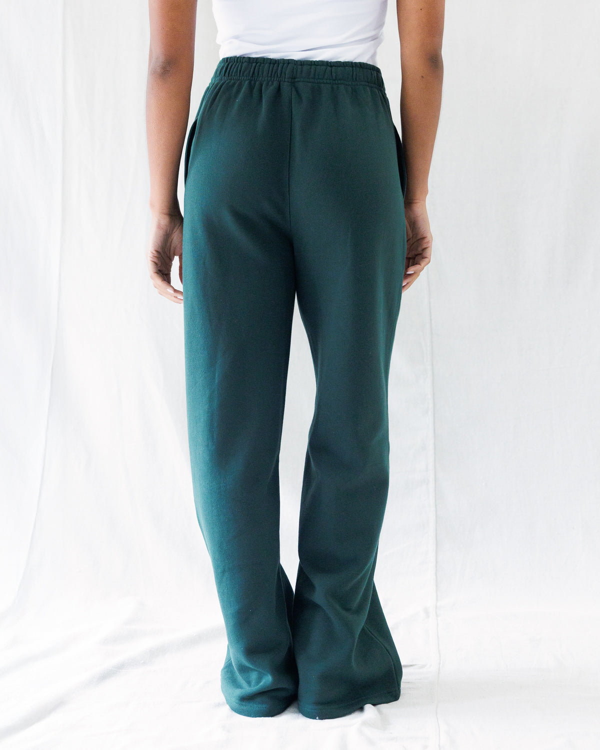 A person shown from the back wearing dark teal wide-leg pants with an elastic waistband, paired with a white top, against a white fabric backdrop.