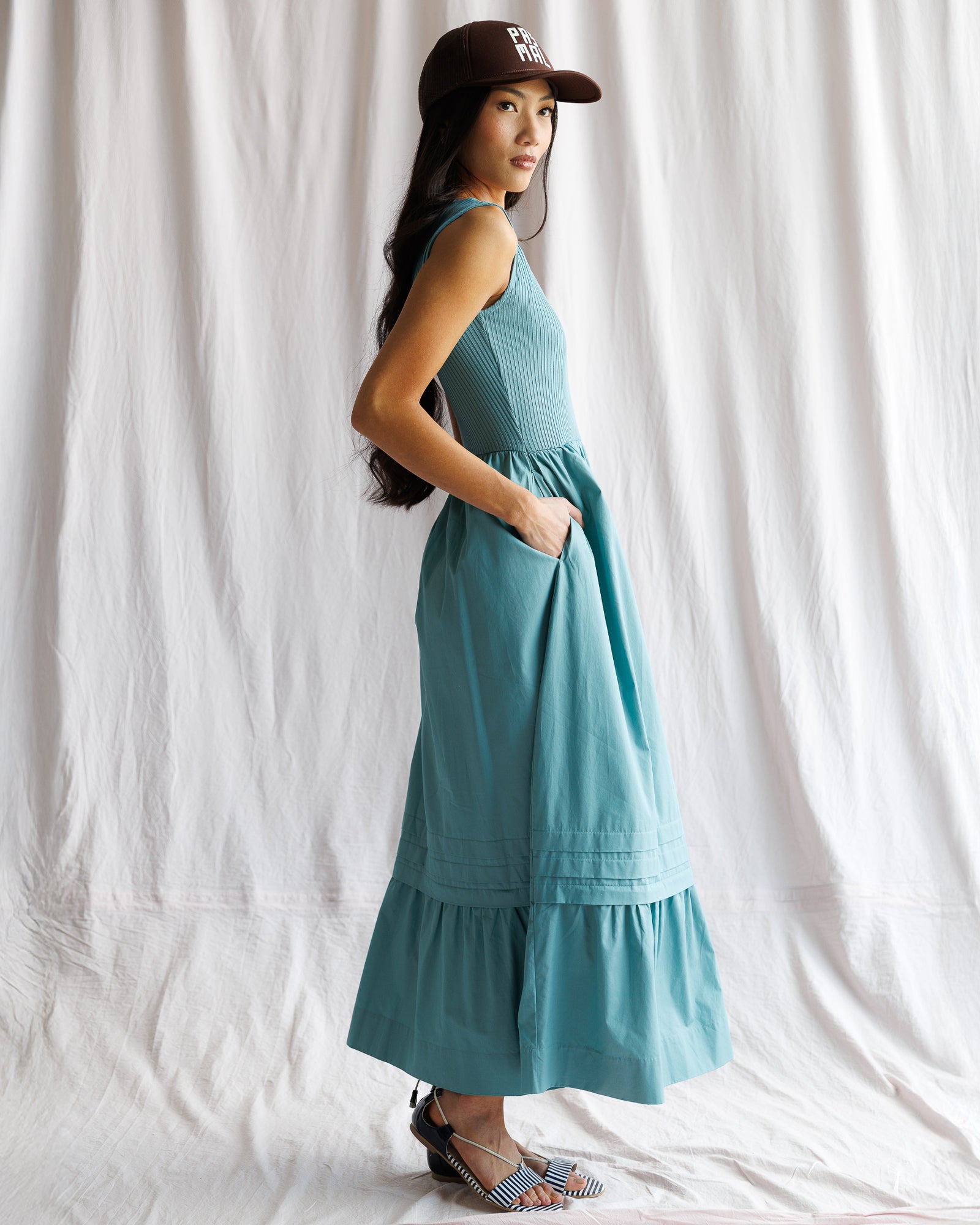 Woman wearing a teal dress and cap against a white curtain background