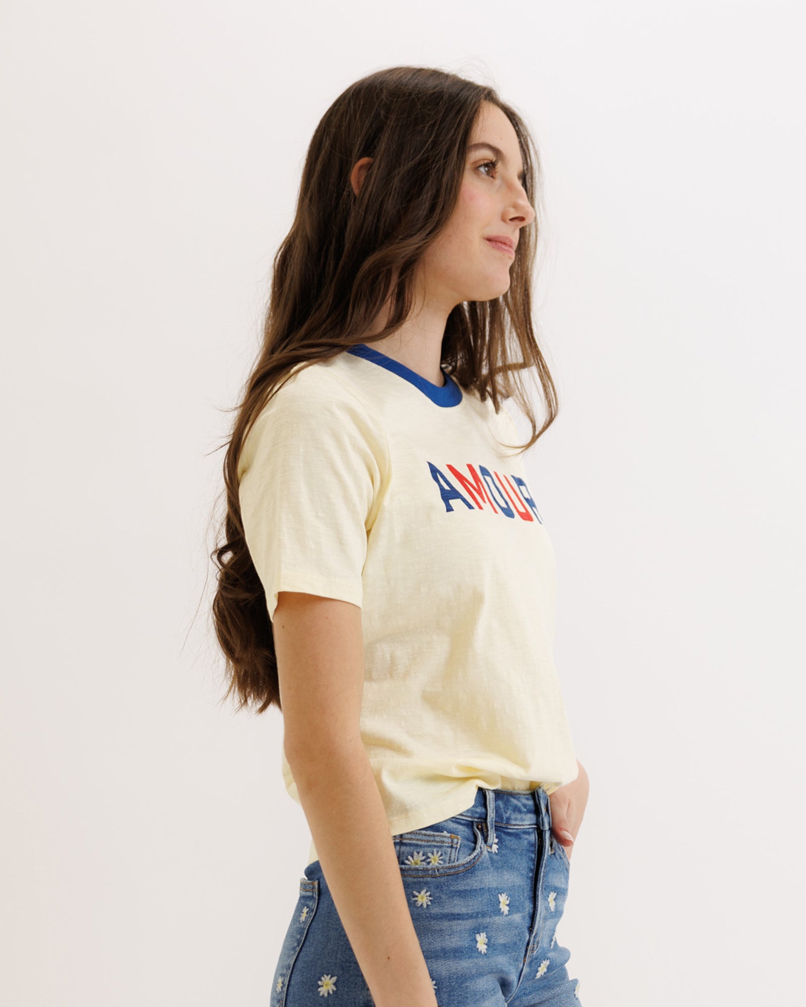 Woman wearing a yellow t-shirt with colorful text and blue jeans on a white background