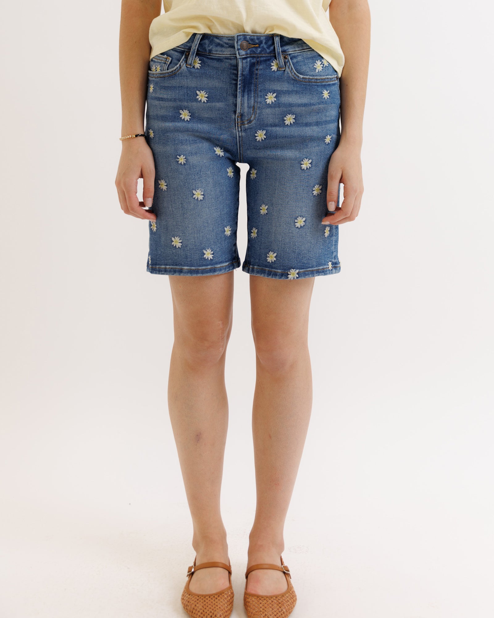 Person wearing blue denim shorts with floral embroidery on a white background