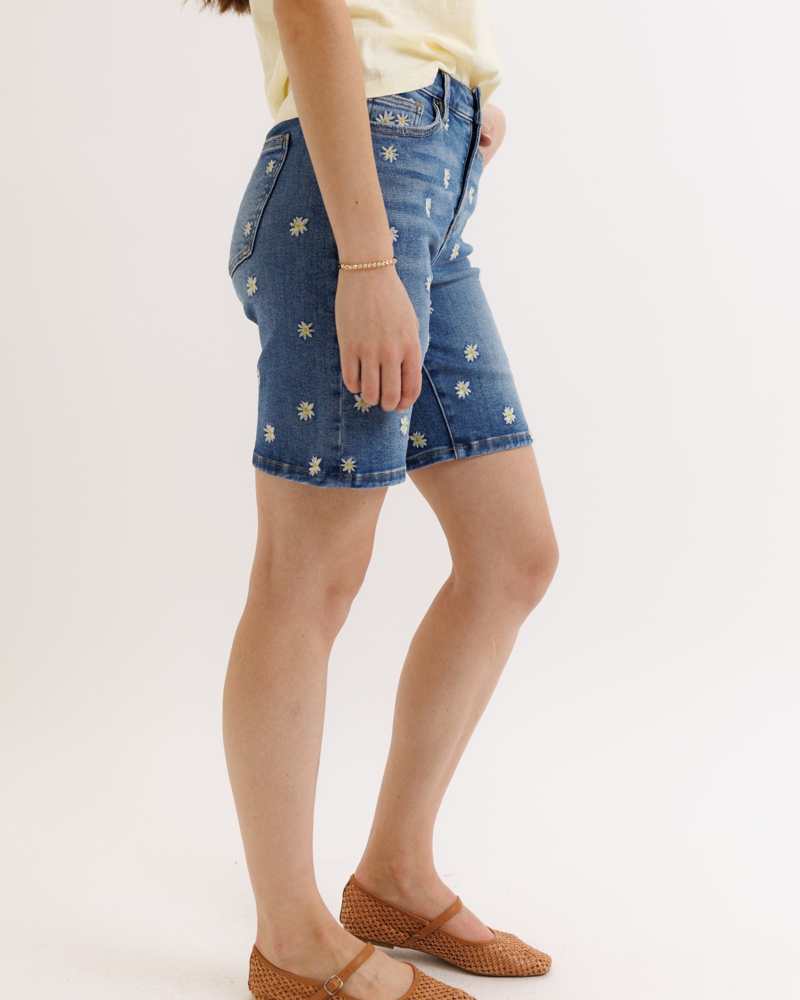 Denim shorts with floral embroidery worn by a person on a white background