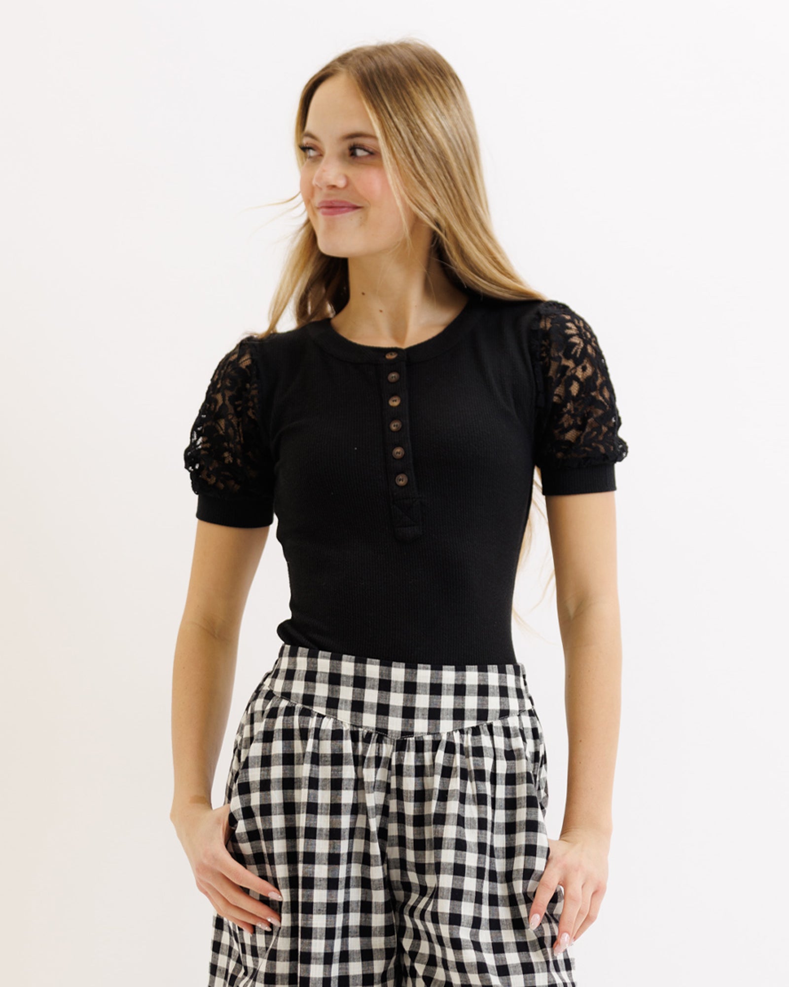 Woman wearing a black top with lace sleeves and checkered pants on a white background