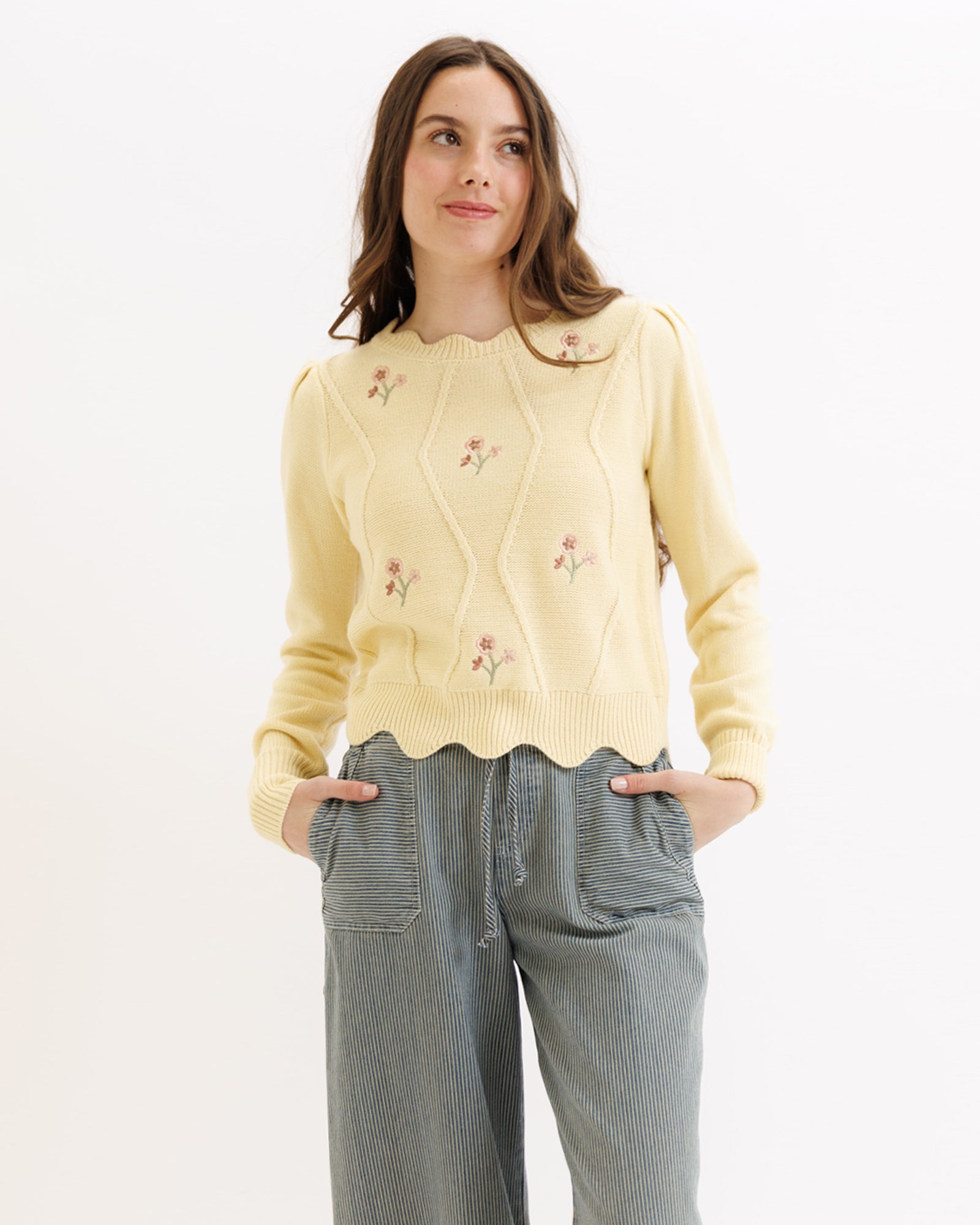 Woman wearing a light yellow sweater with floral embroidery on a white background