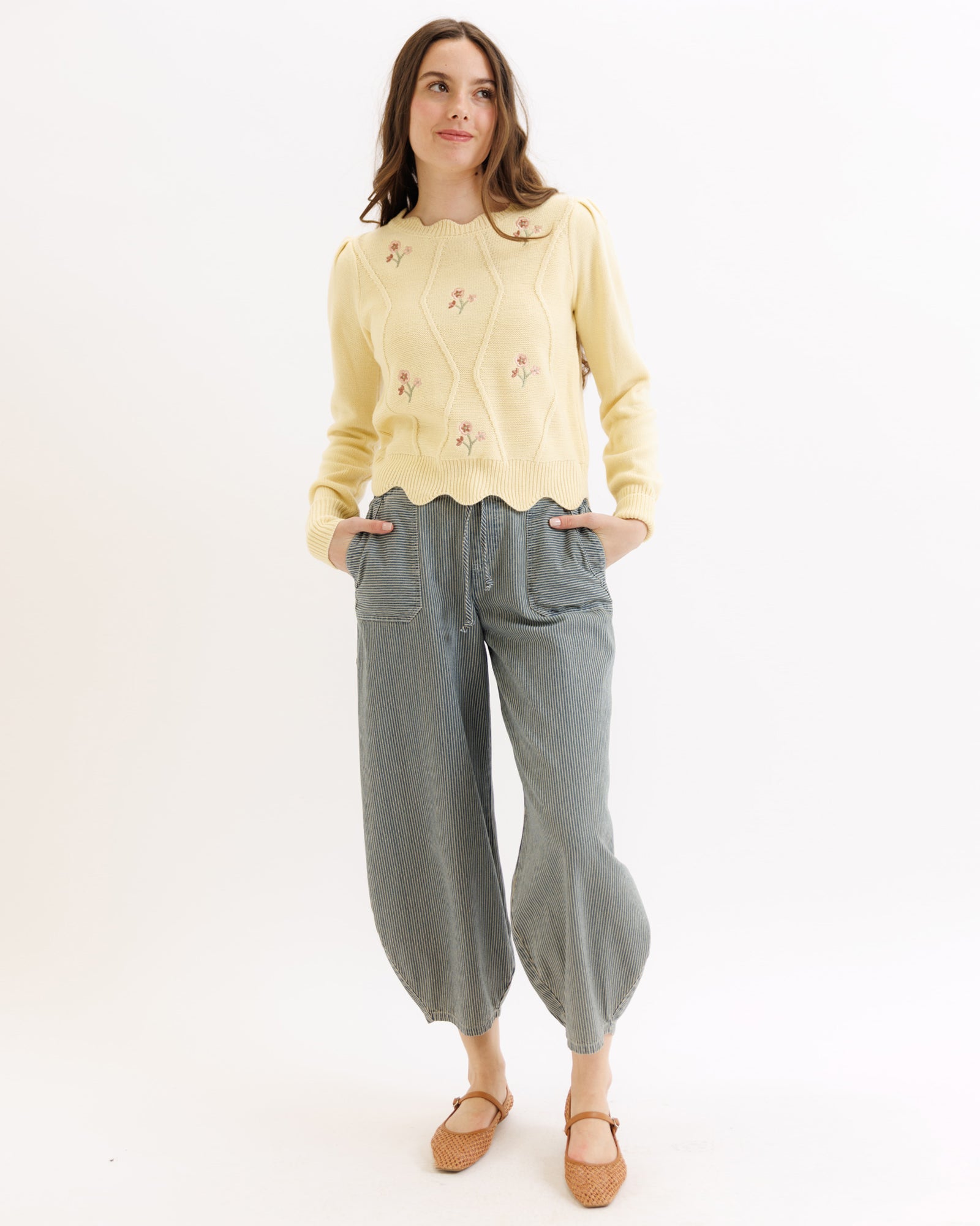 Woman wearing a yellow sweater and gray pants on a white background