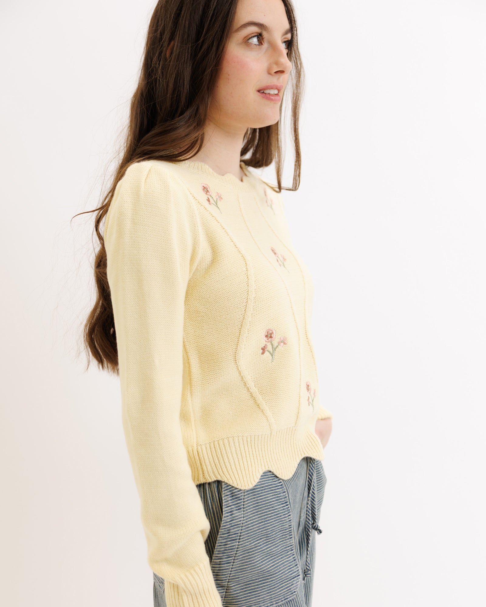 Woman wearing a light yellow cardigan with floral embroidery on a plain background