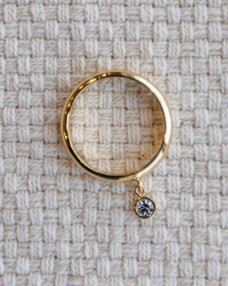 Gold ring with a small gemstone on a textured beige fabric background