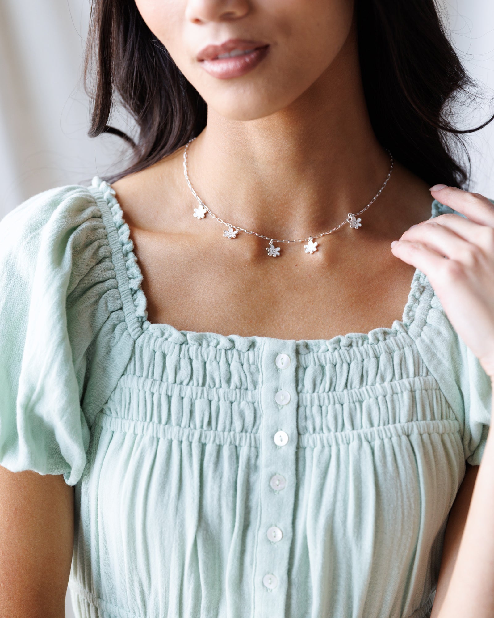Woman wearing a light green top and a delicate necklace with small flowers.