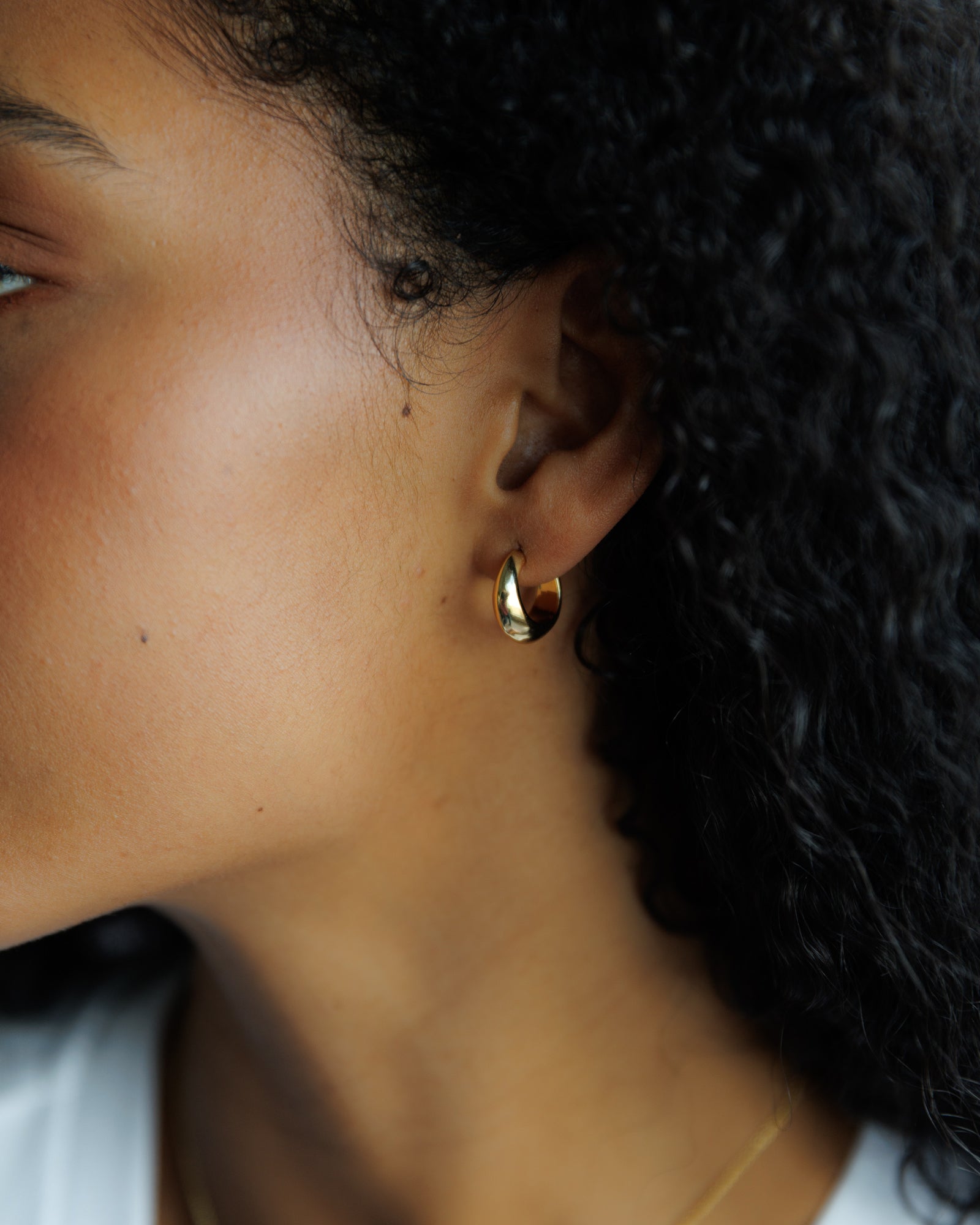 Close-up of a person wearing a gold earring with a blurred background