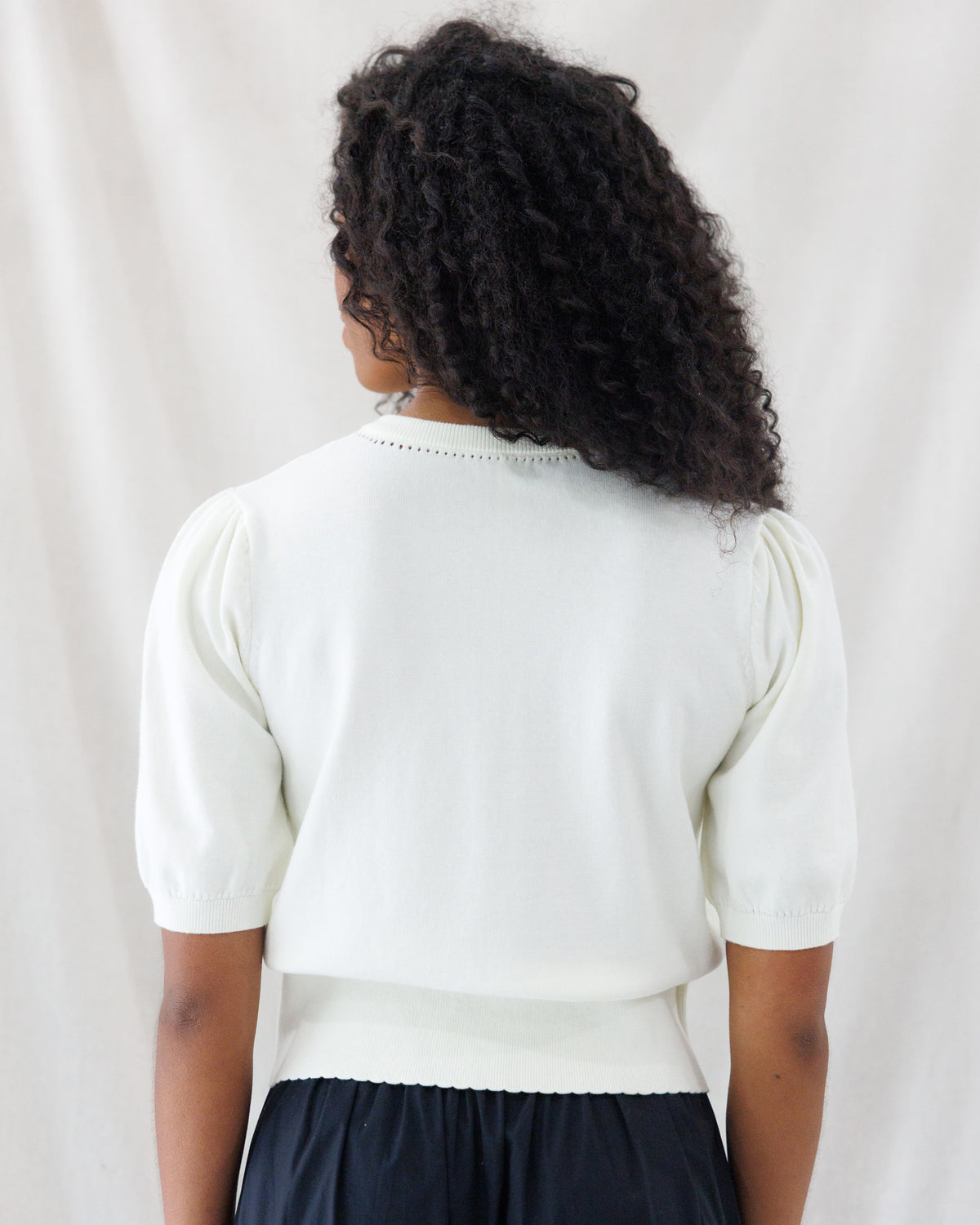 Back view highlighting the delicate pointelle stitch detail along the crew neckline, subtle shoulder gathers on the elbow-length sleeves, and fitted ribbed hem of the cream knit sweater top.