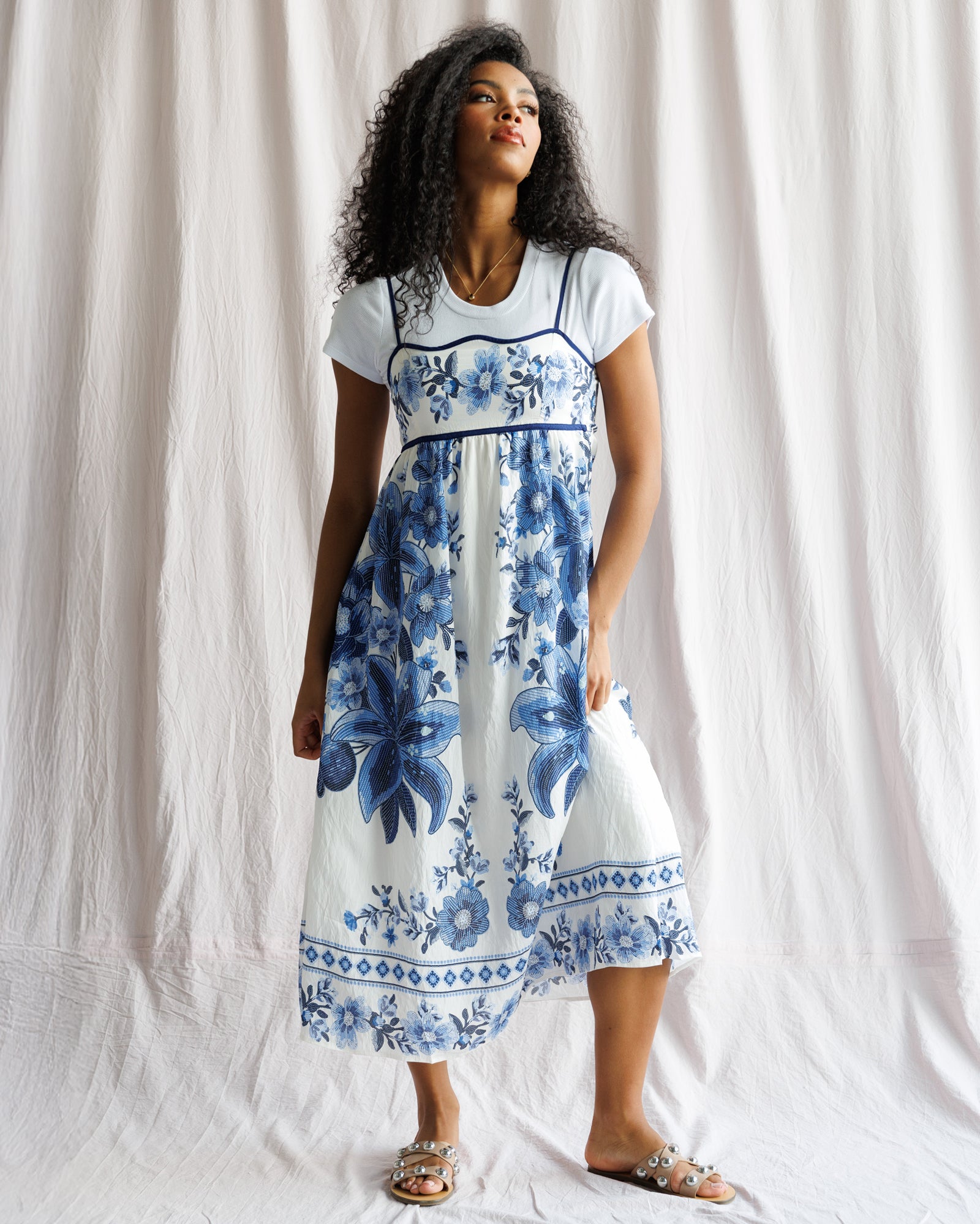 Woman wearing a white dress with blue floral patterns against a white curtain background
