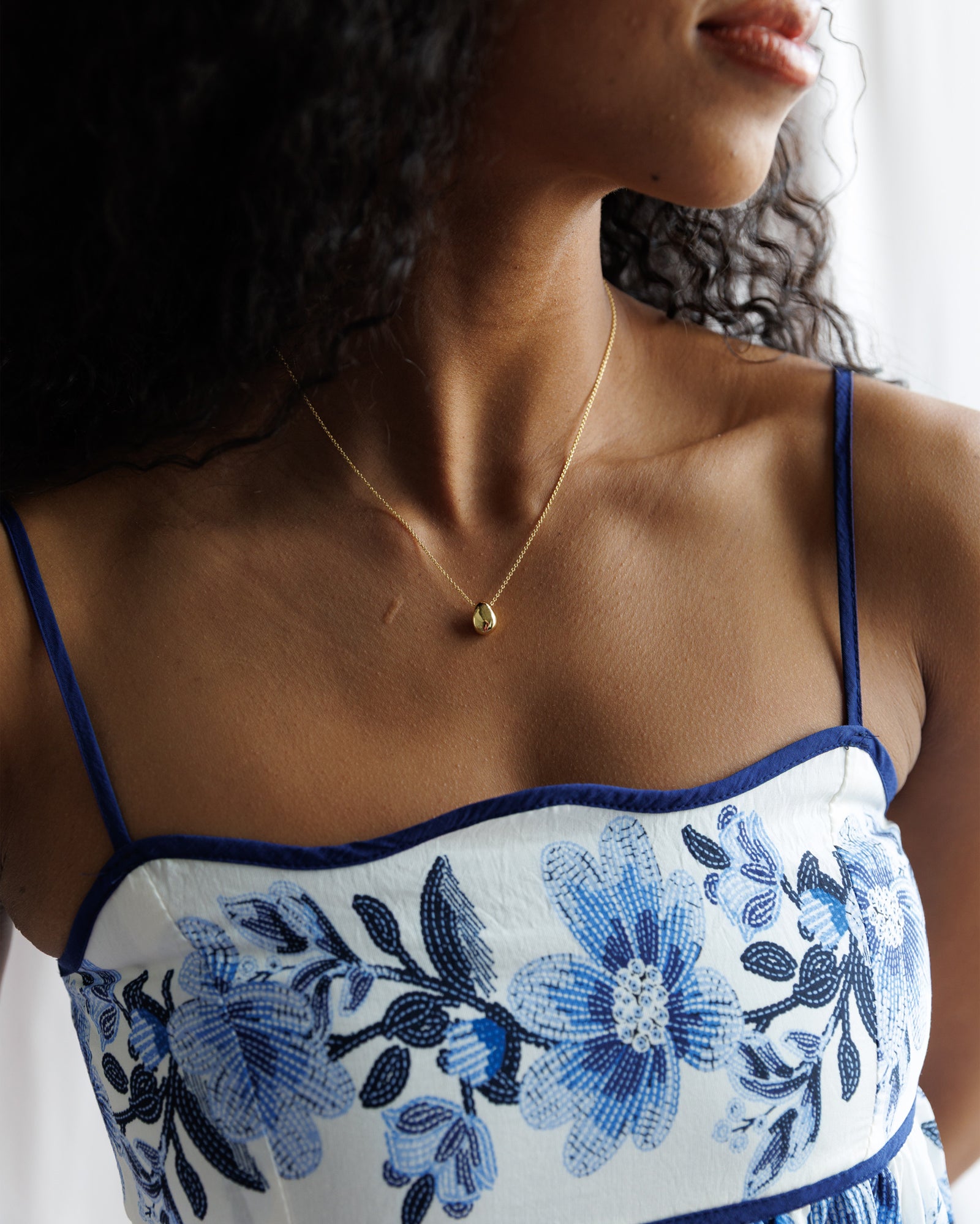 Woman wearing a white dress with blue floral embroidery and a gold necklace.