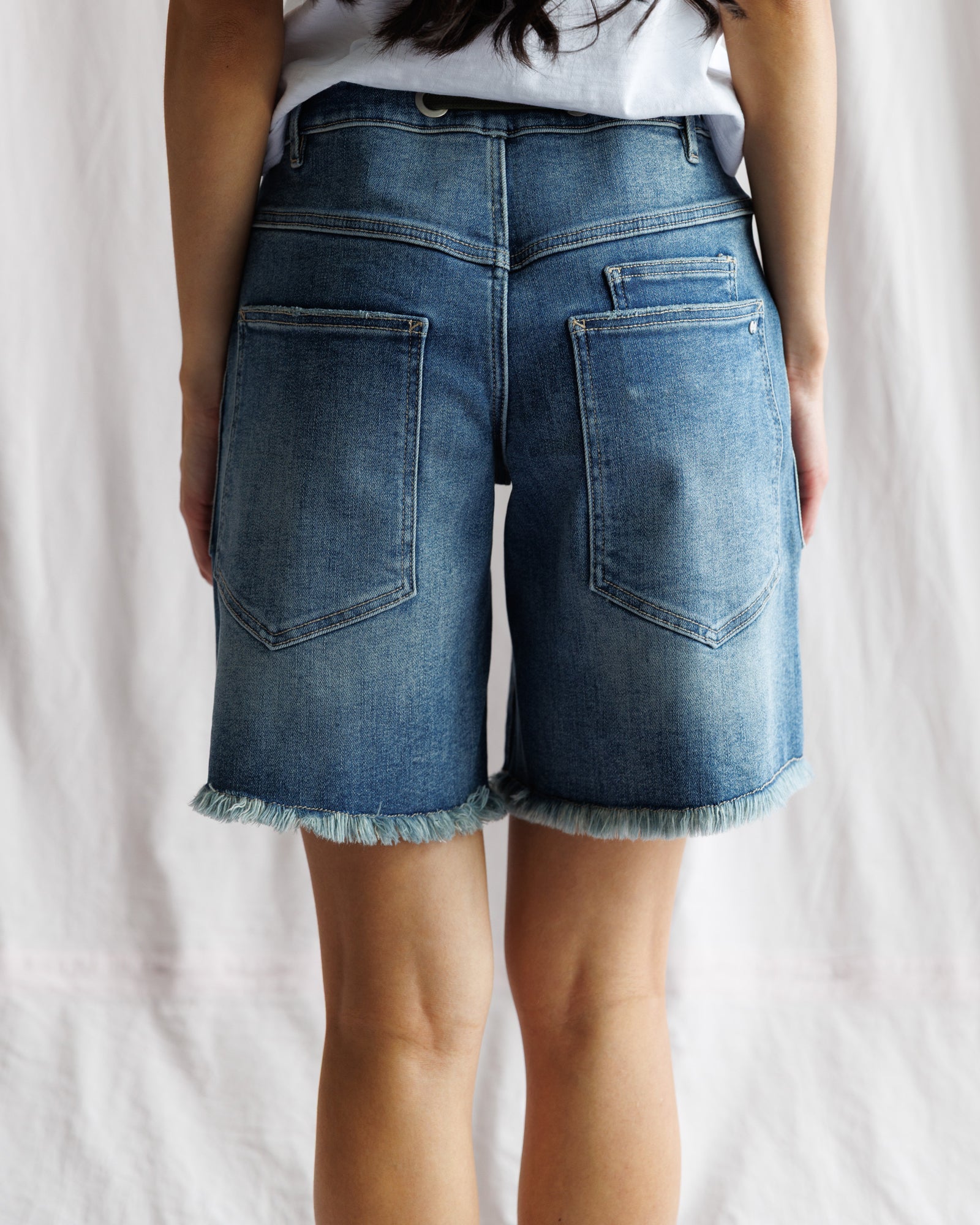 Blue denim shorts worn by a person on a plain background