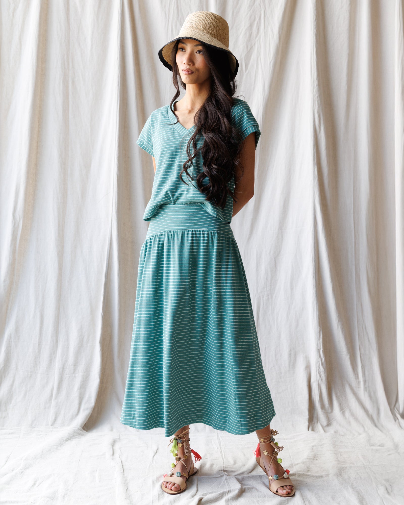 Woman wearing a teal dress and hat against a white curtain background