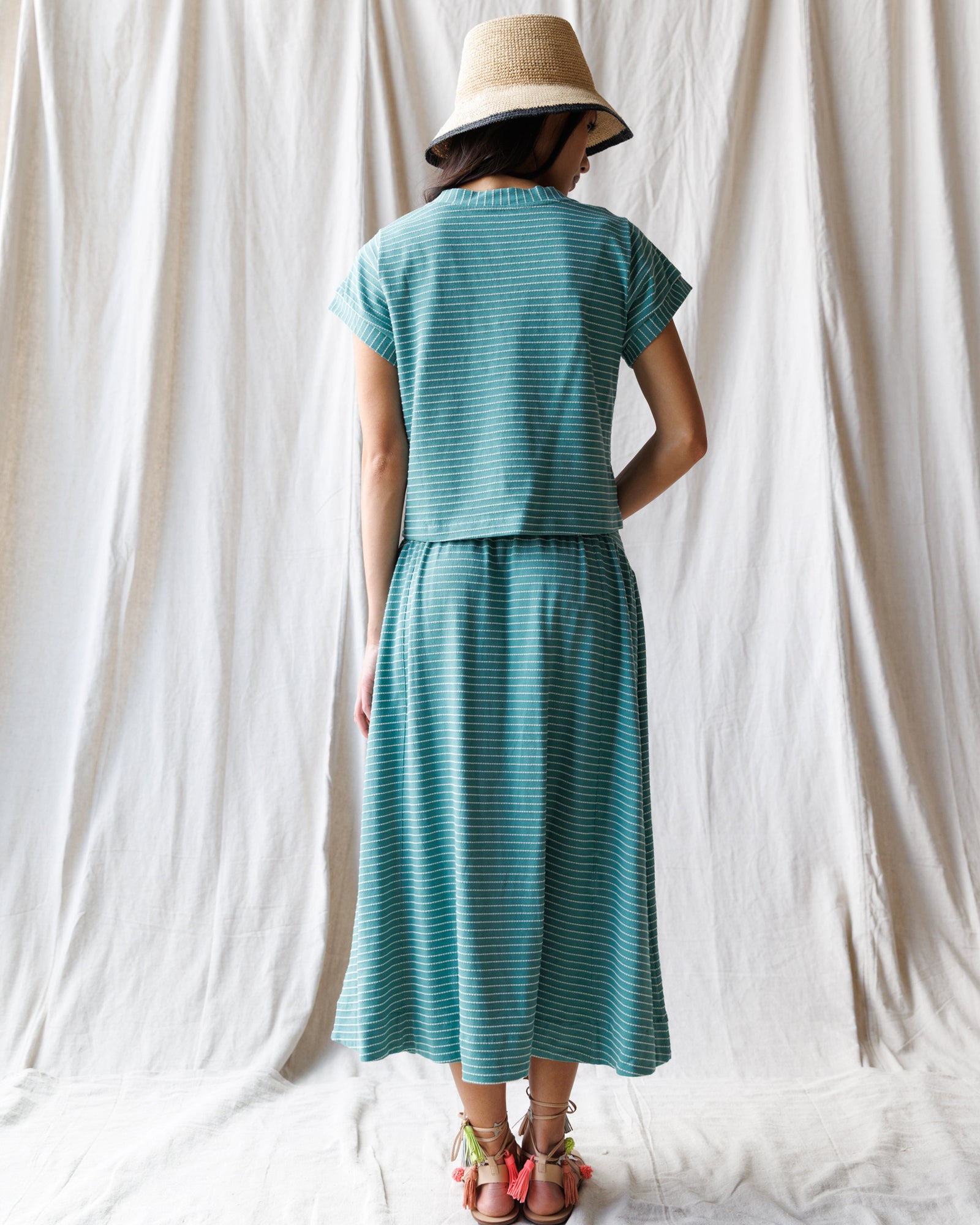 Person wearing a teal dress and hat standing against a white curtain