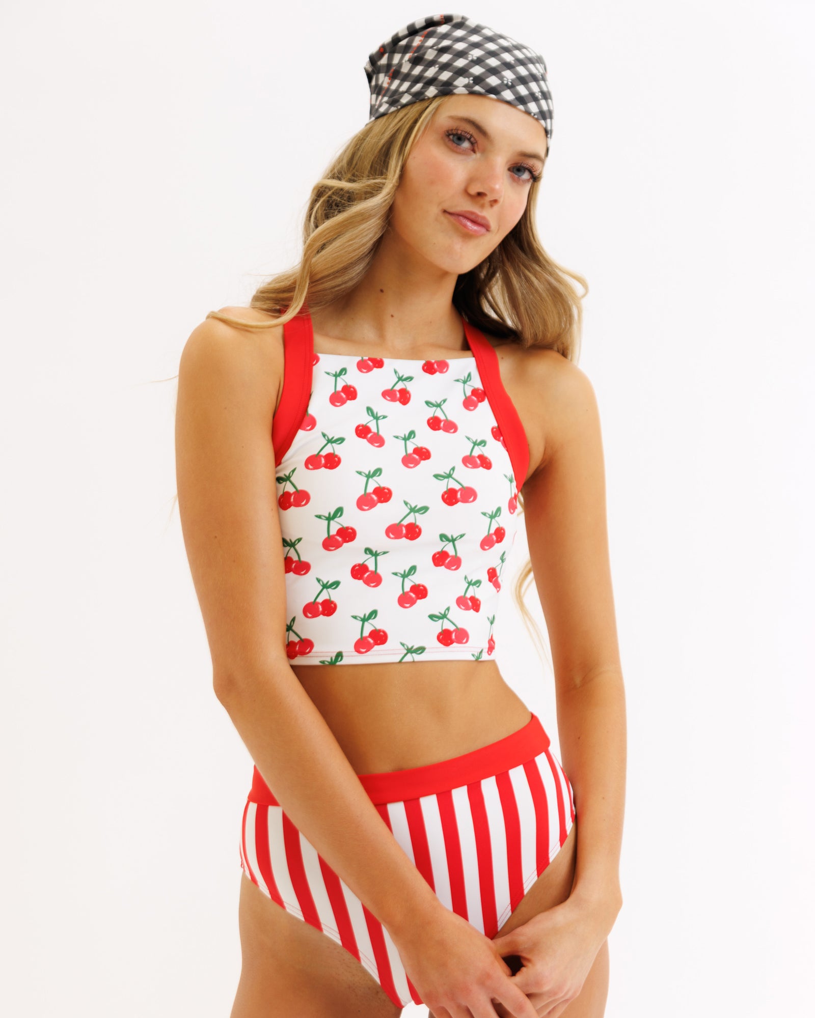 Woman wearing a cherry-patterned bikini top and red and white striped shorts on a plain background