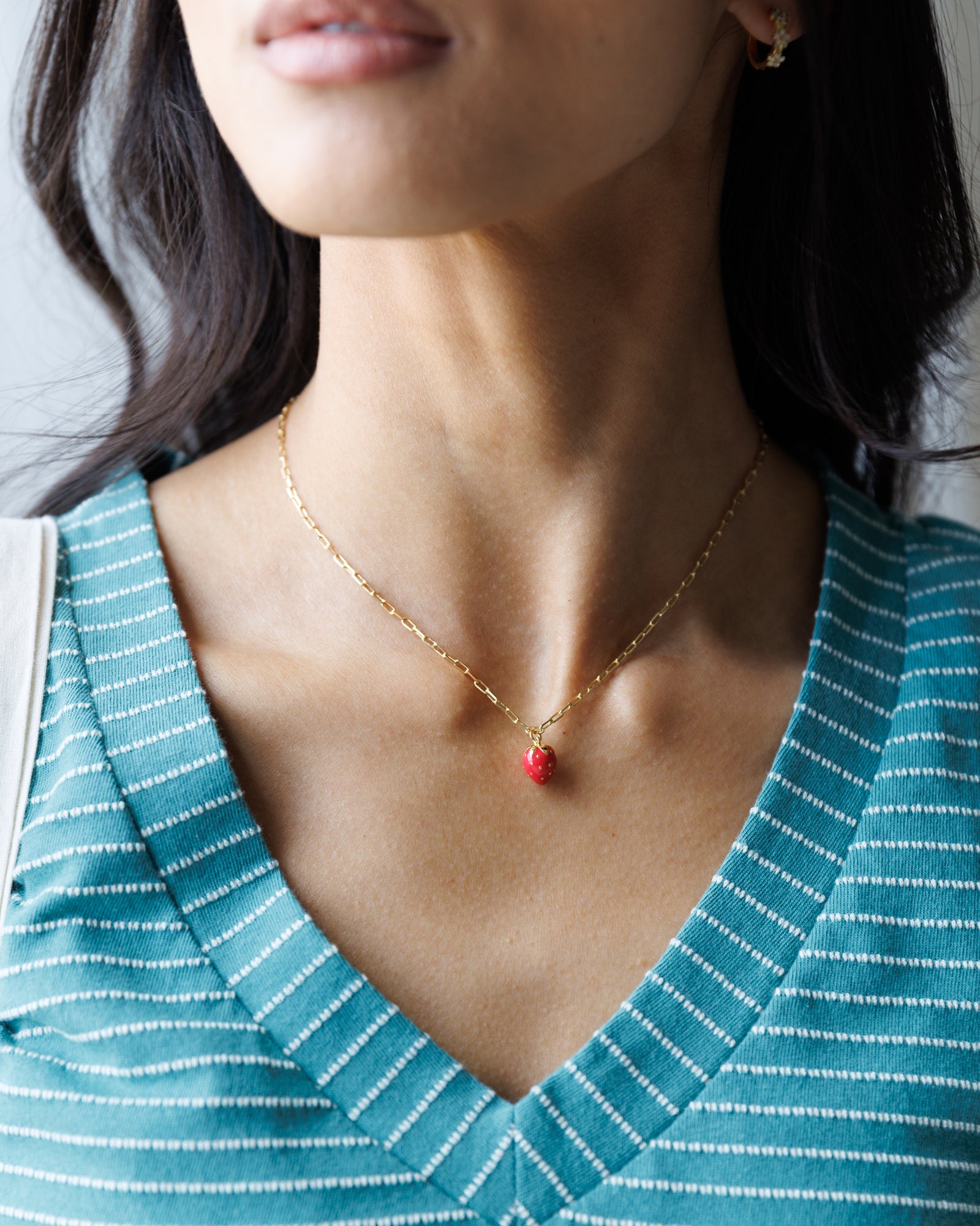 Woman wearing a gold necklace with a red pendant, against a neutral background