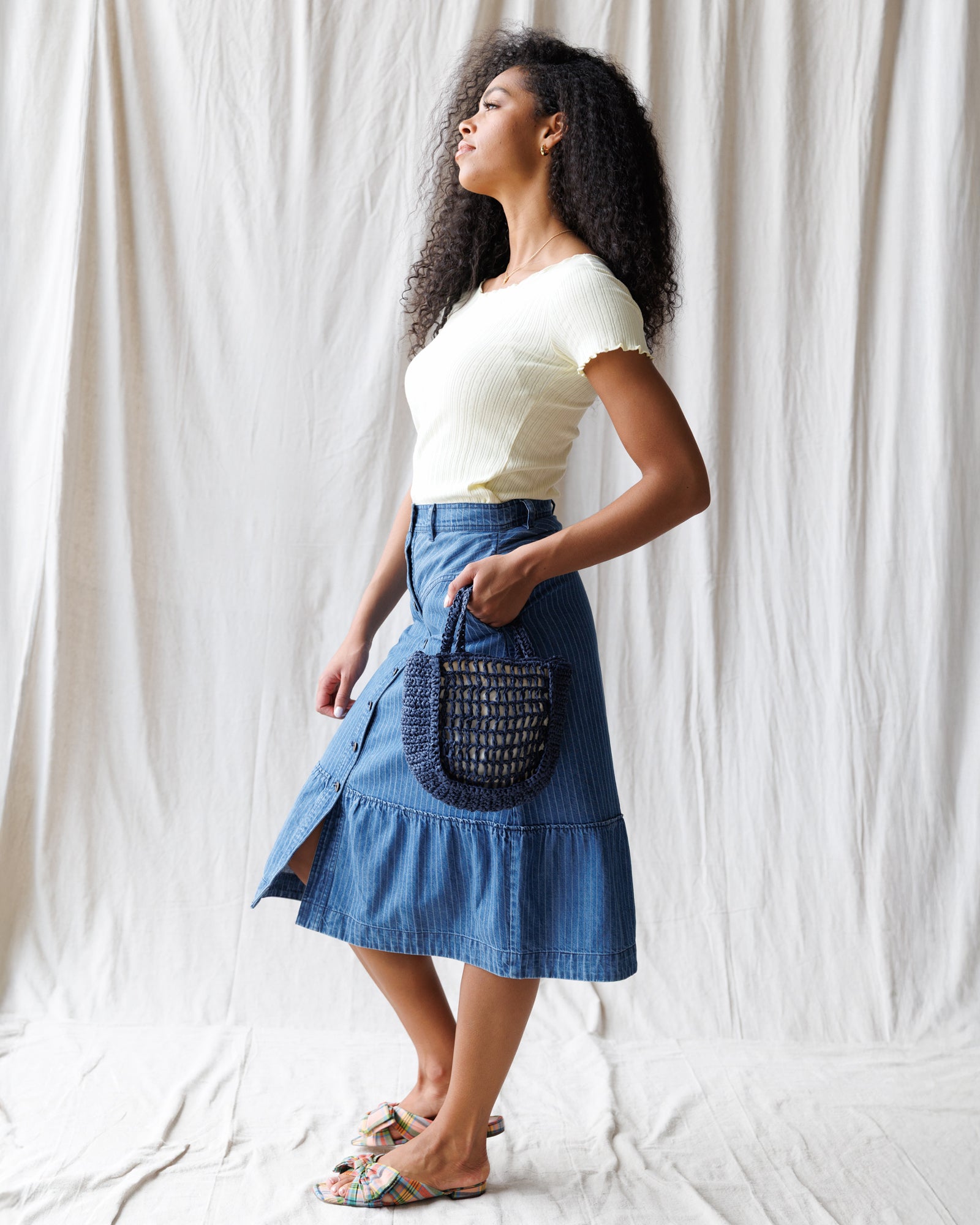 Woman wearing a white top and blue denim skirt holding a blue handbag against a white background