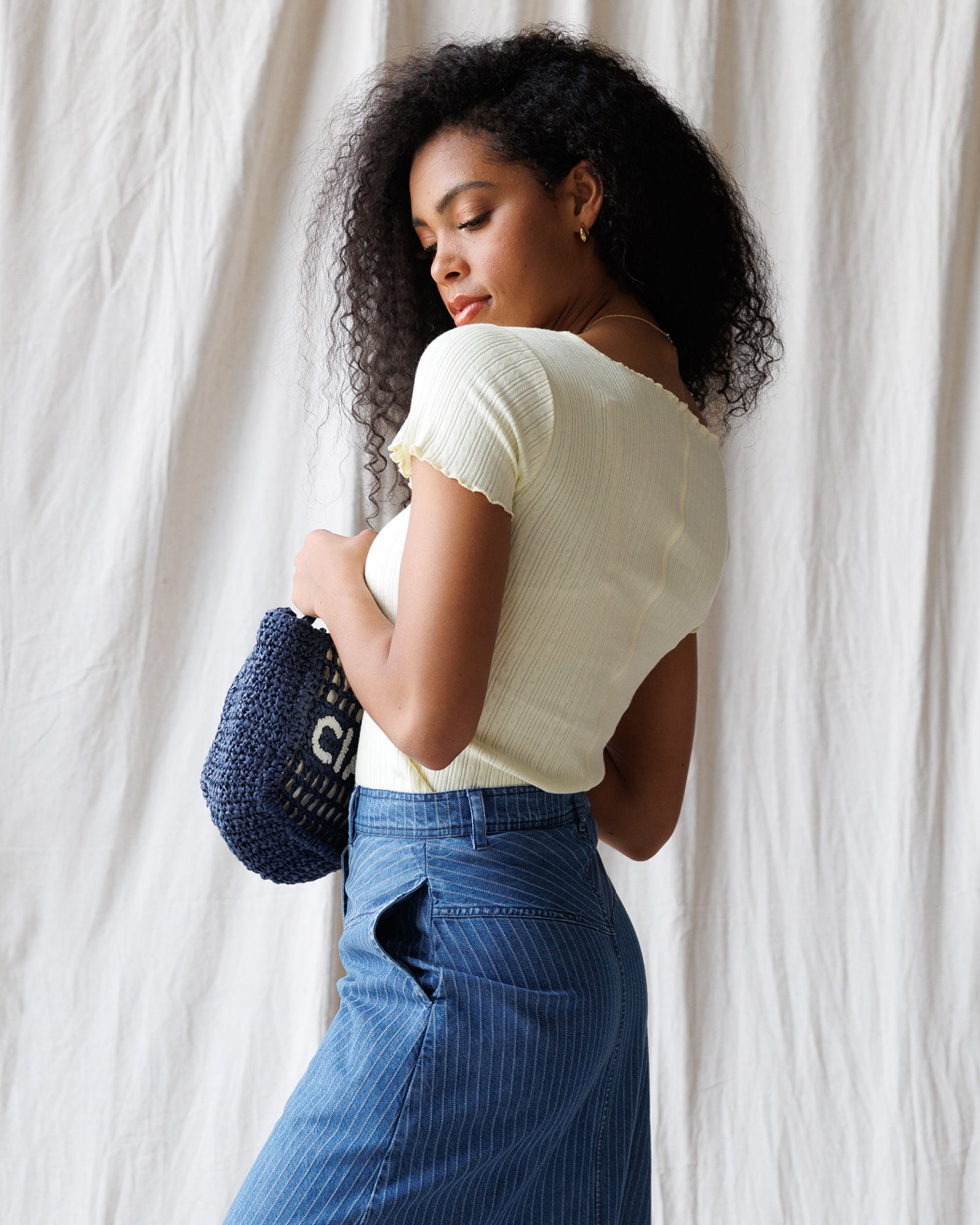 Woman holding a blue handbag against a white curtain background