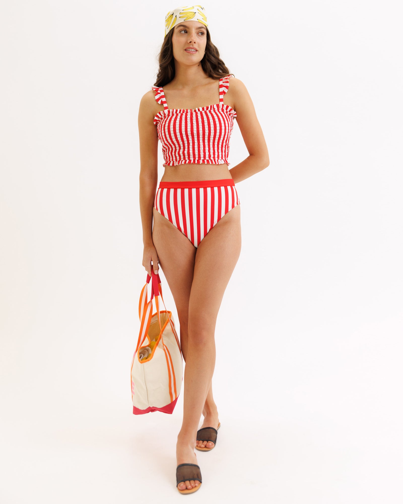 Woman wearing a red and white striped bikini holding a bag on a white background
