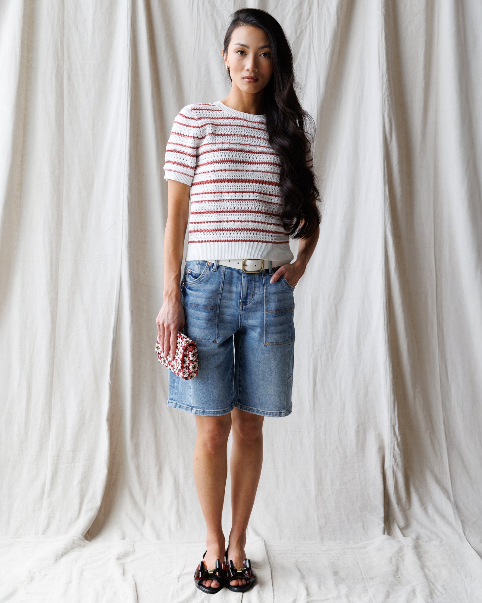 Woman wearing a striped shirt and denim shorts against a white curtain background