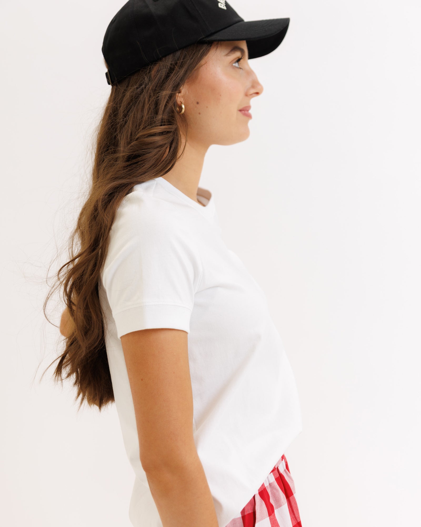 Woman wearing a black cap and white t-shirt with a red and white striped skirt on a plain background