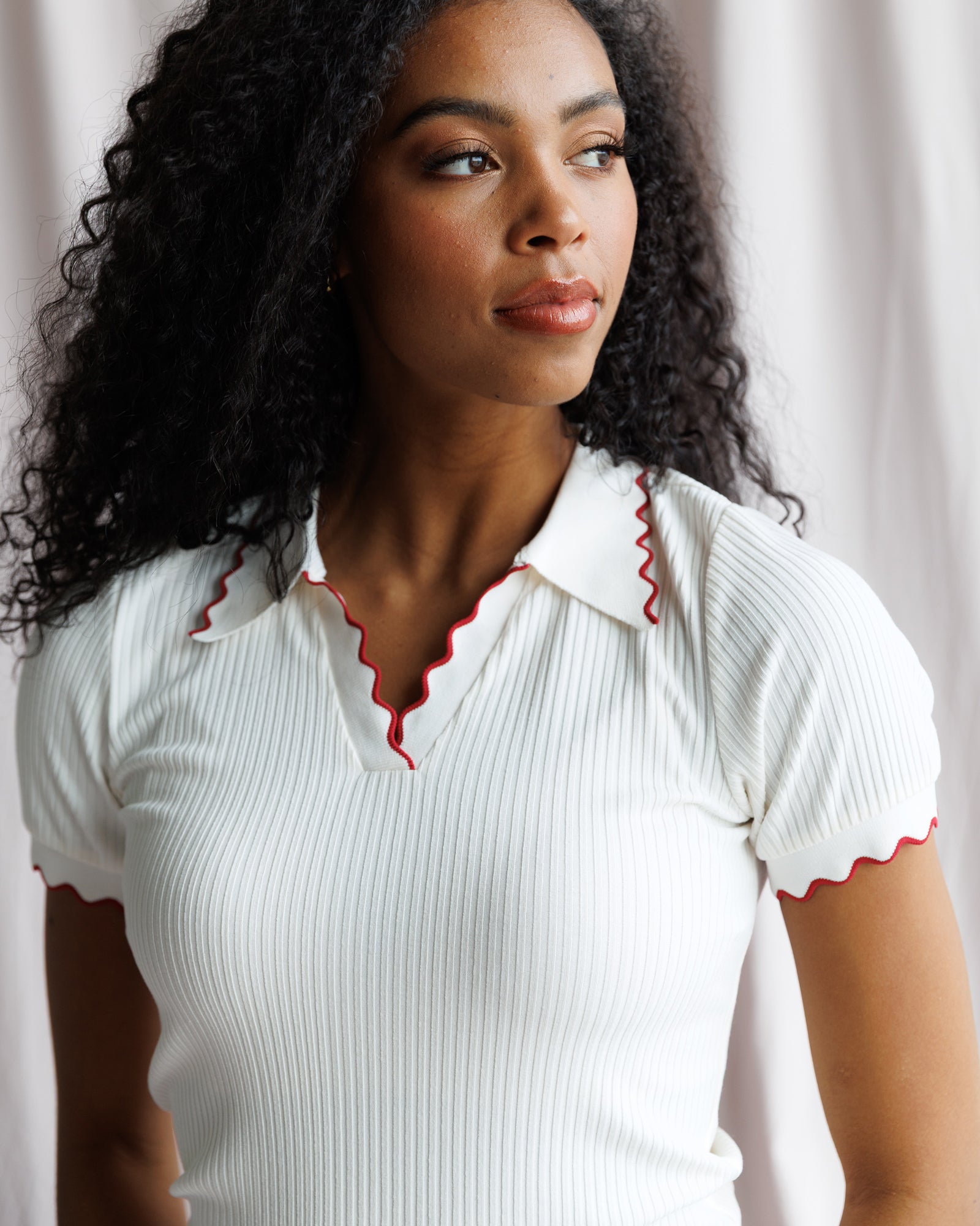 Woman wearing a white ribbed top with red trim against a neutral background