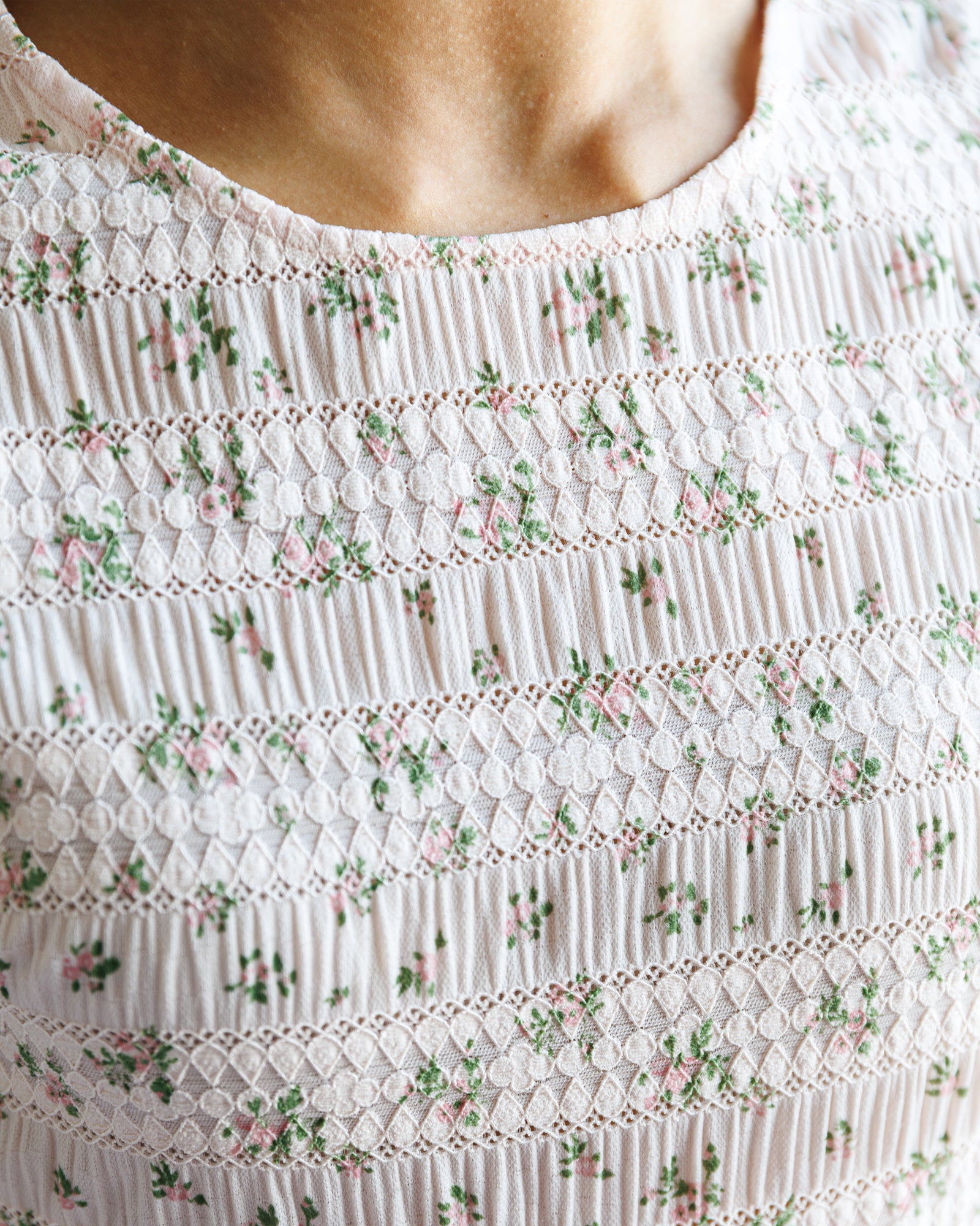 Close-up of a white dress with floral patterns and smocked details.