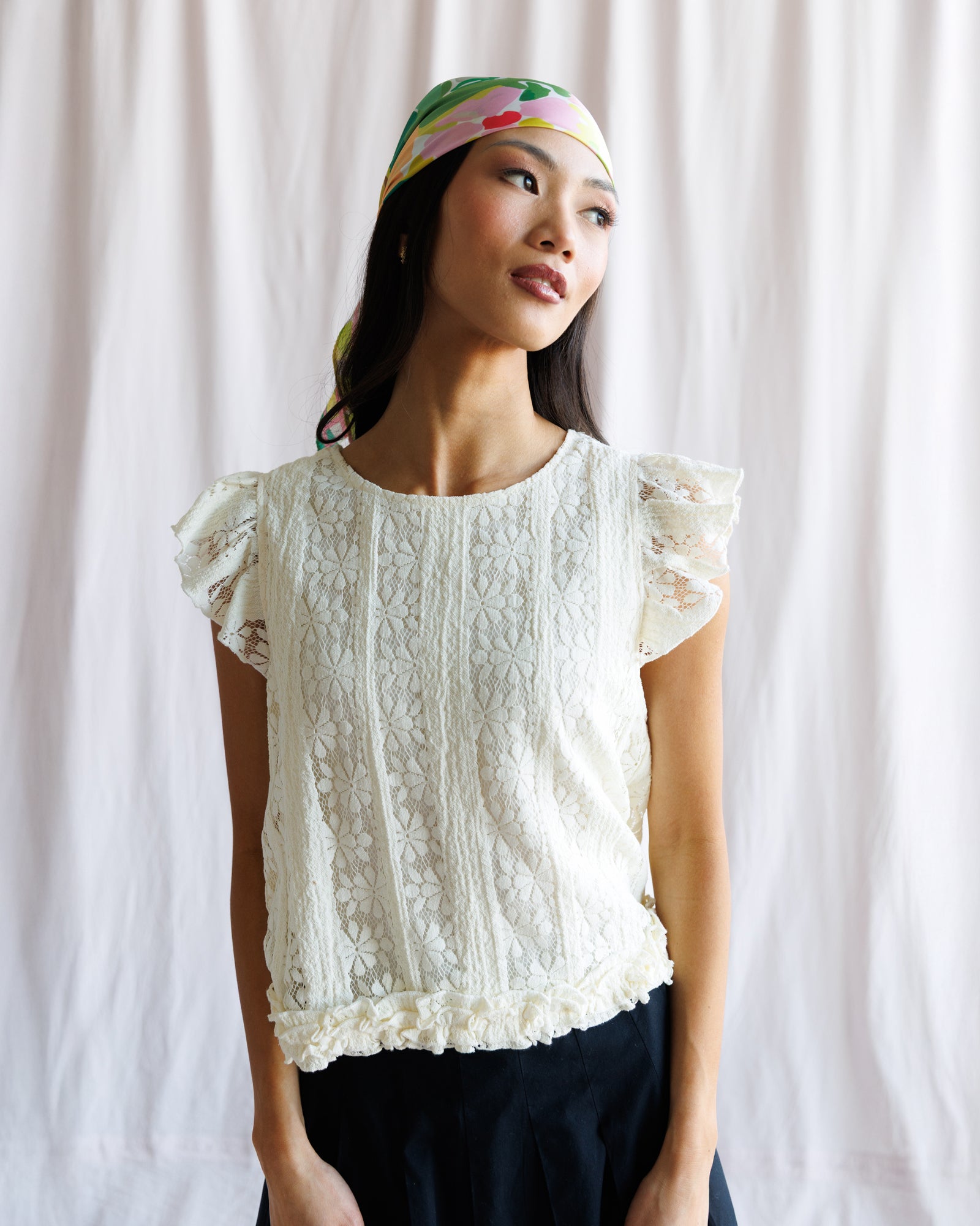 Woman wearing a white lace top and colorful headband against a plain background