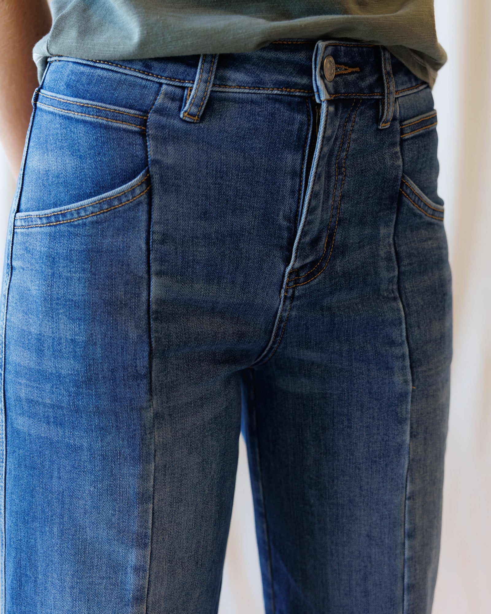 Close-up of a person wearing blue denim jeans with a slightly faded wash, showing the front waistband, belt loops, and side pockets.