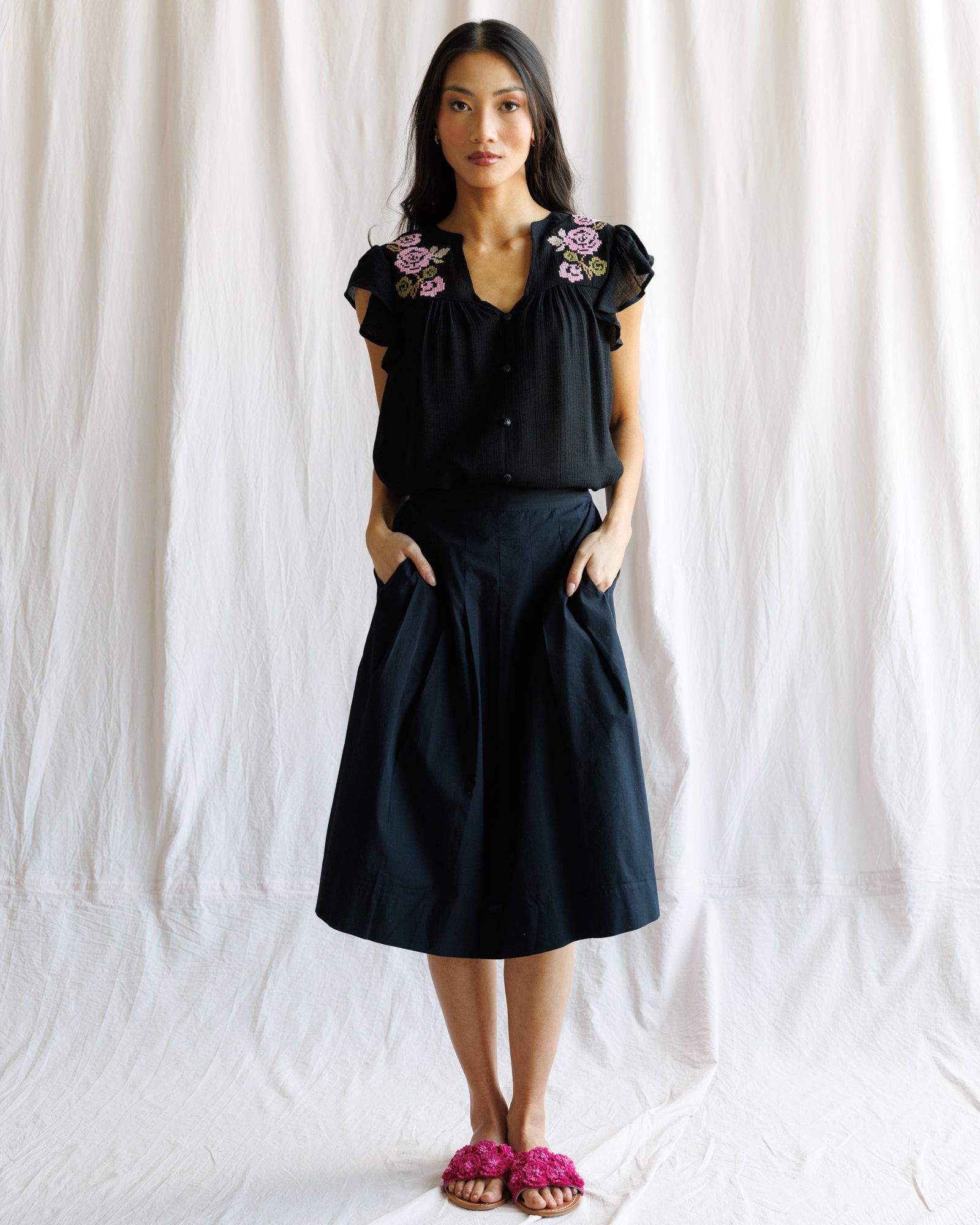 Woman wearing a black blouse with floral embroidery and a black skirt against a white background