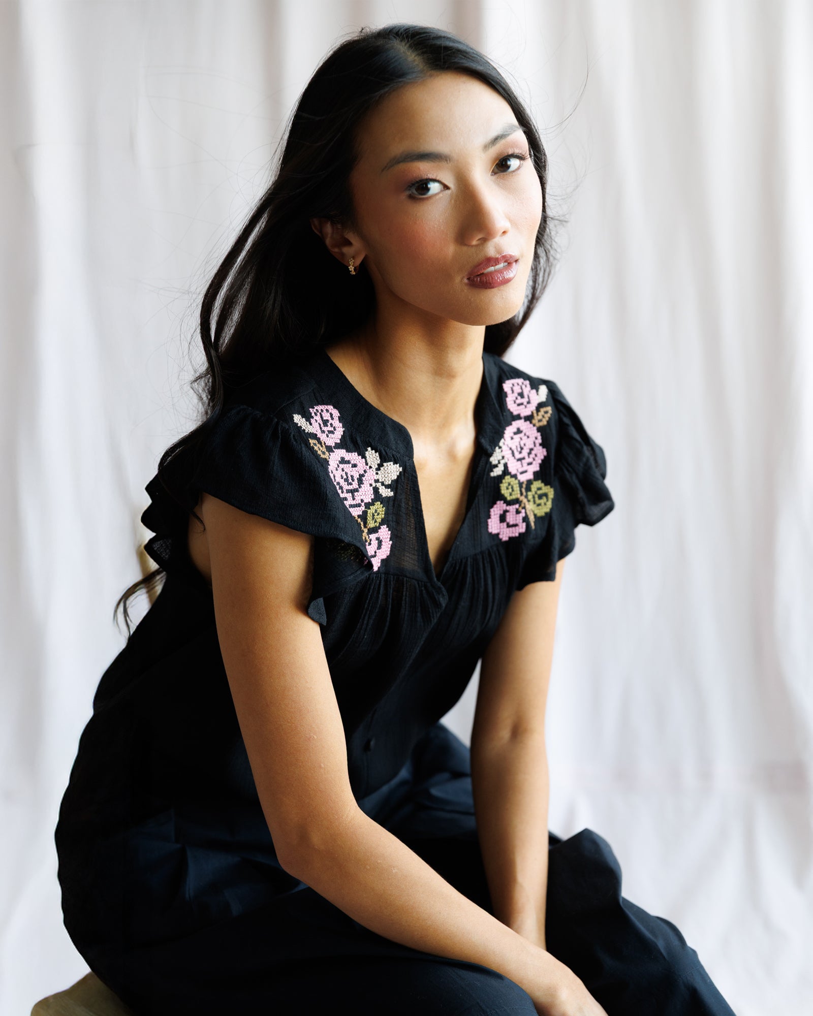 Woman wearing a blacktop with floral embroidery against a white curtain background