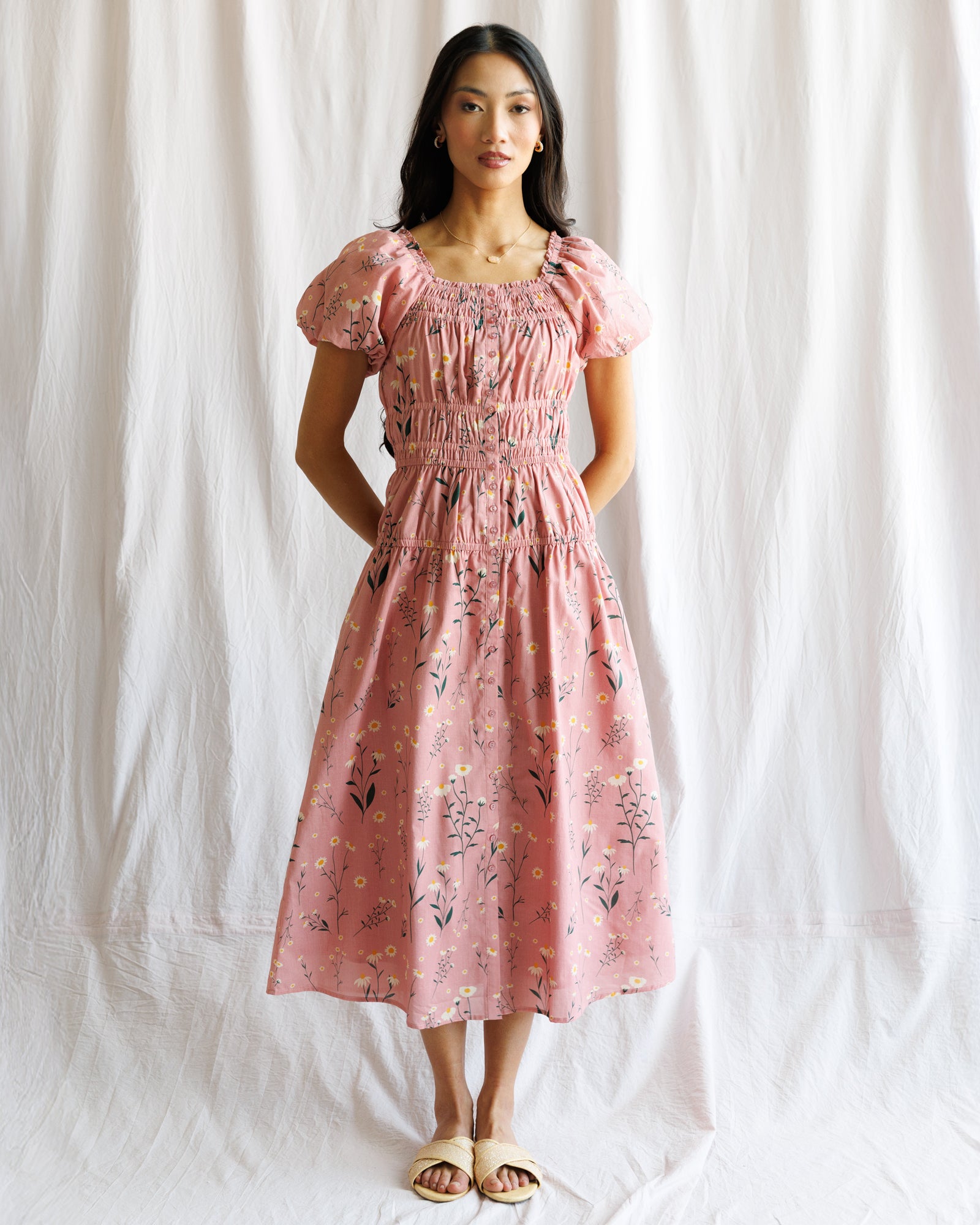 Woman wearing a pink floral dress against a white curtain background