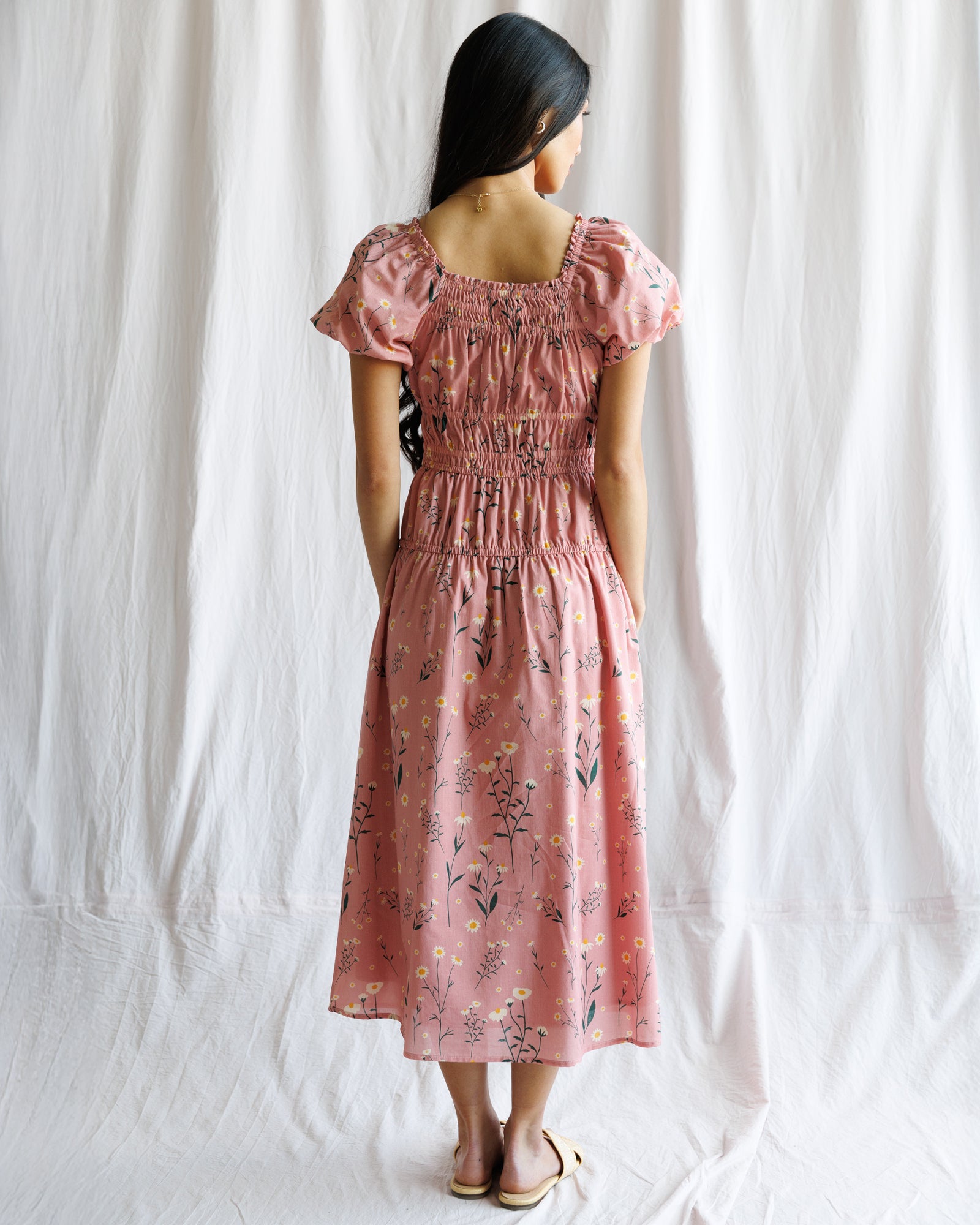 Woman wearing a pink floral dress against a white curtain background