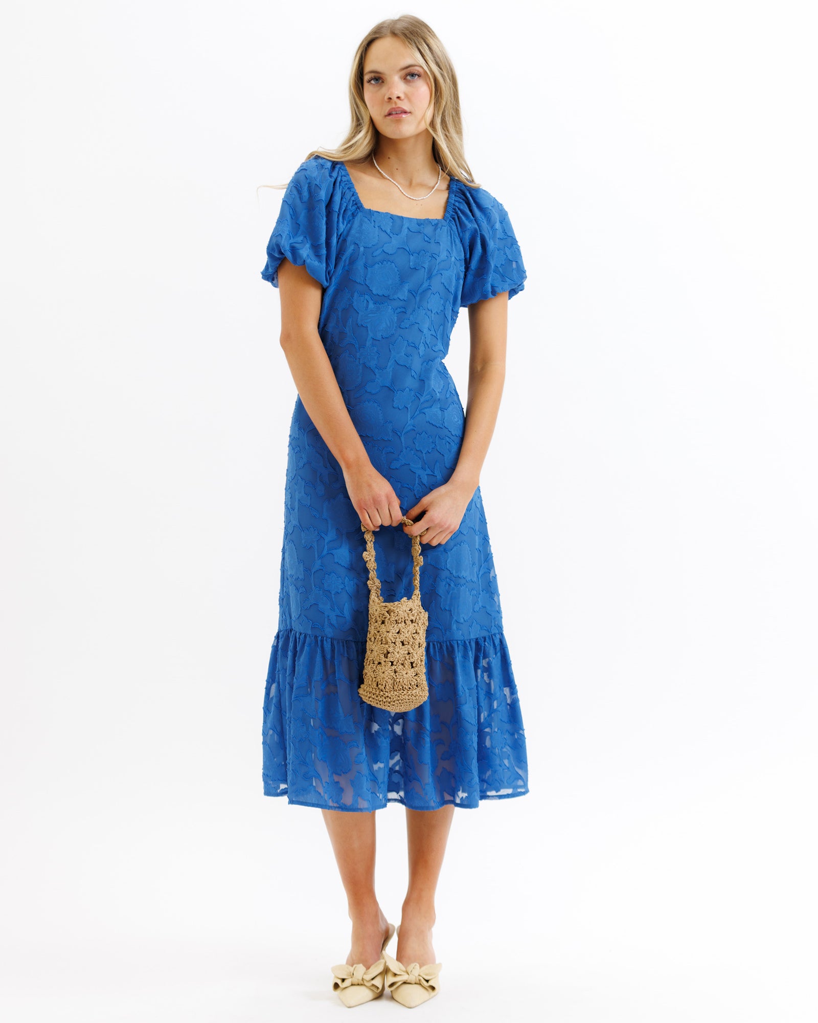 Woman wearing a blue dress holding a straw bag on a white background