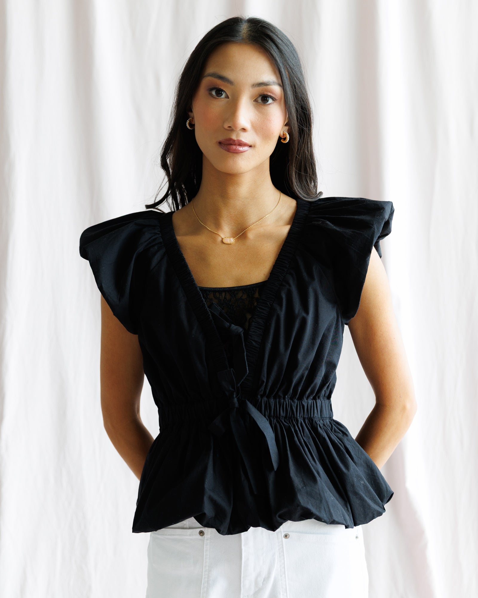 Woman wearing a black top with ruffled sleeves against a white curtain background