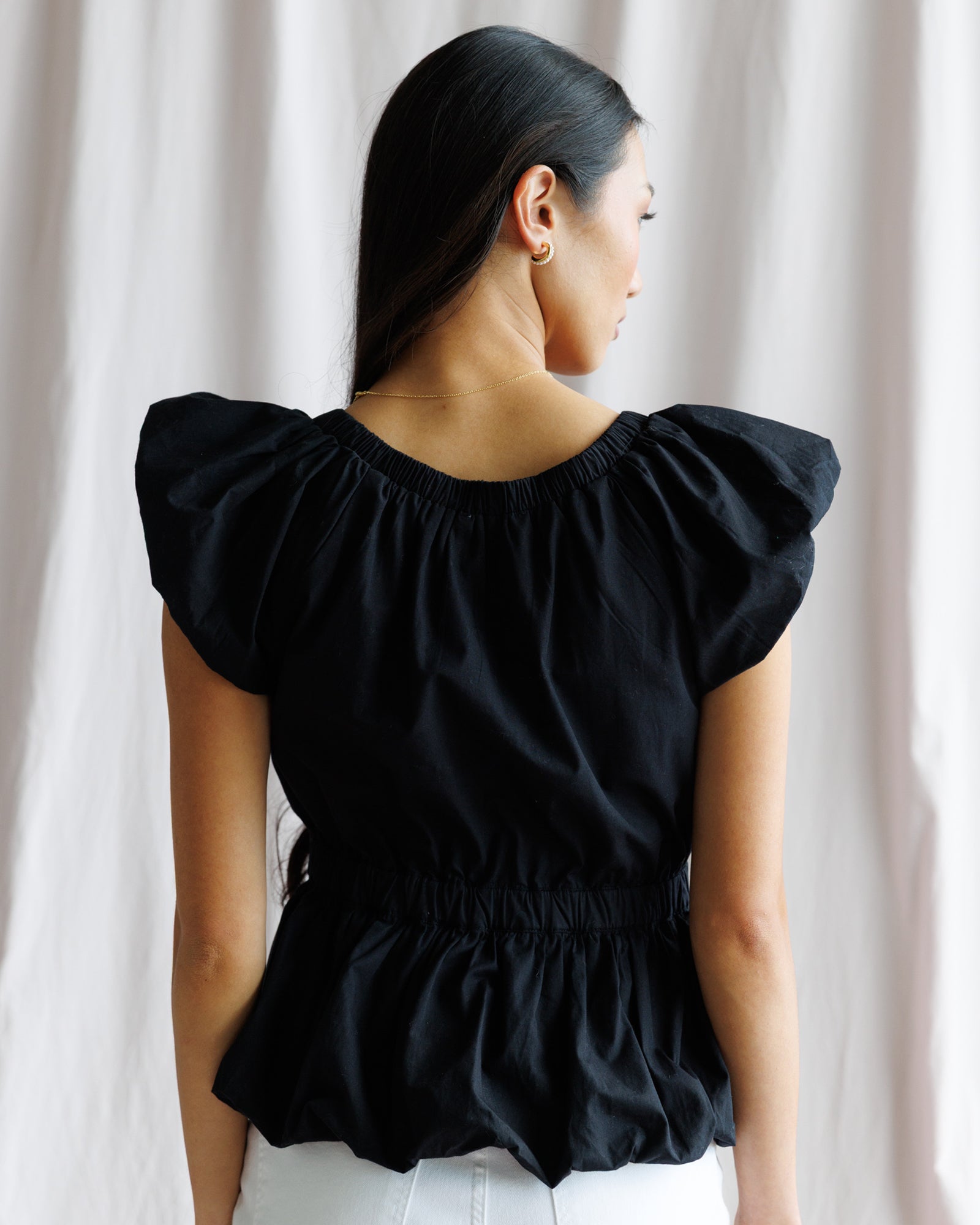 Woman wearing a black blouse with ruffled sleeves against a white curtain background
