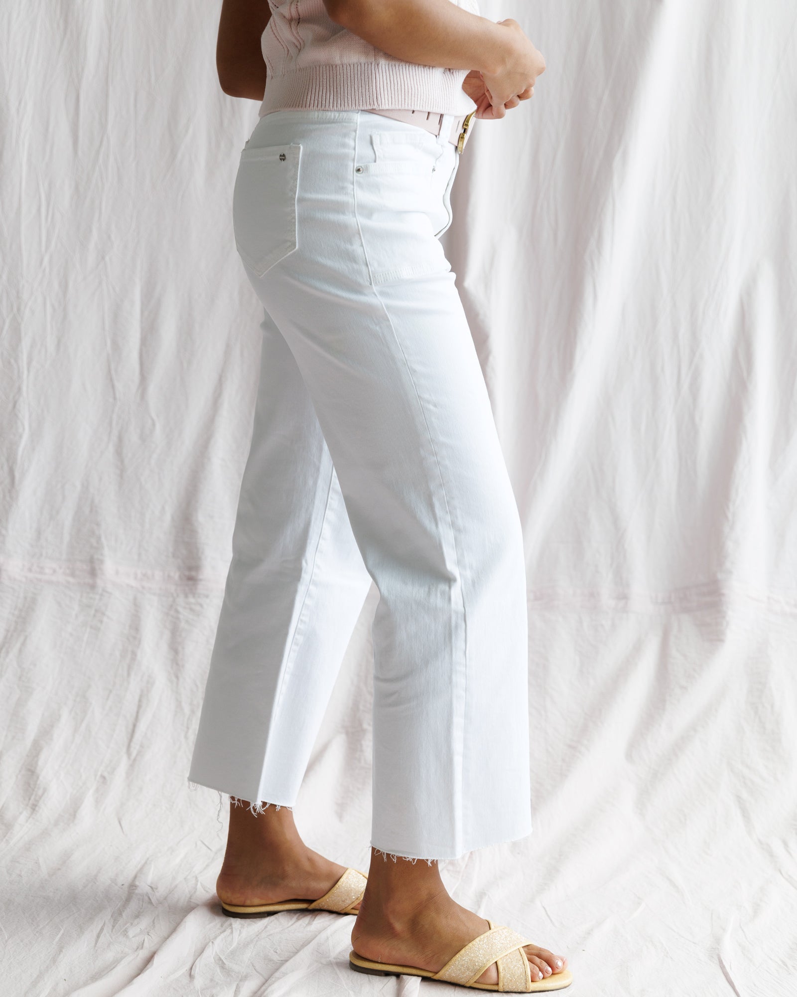 Person wearing light blue jeans and a white top against a plain background