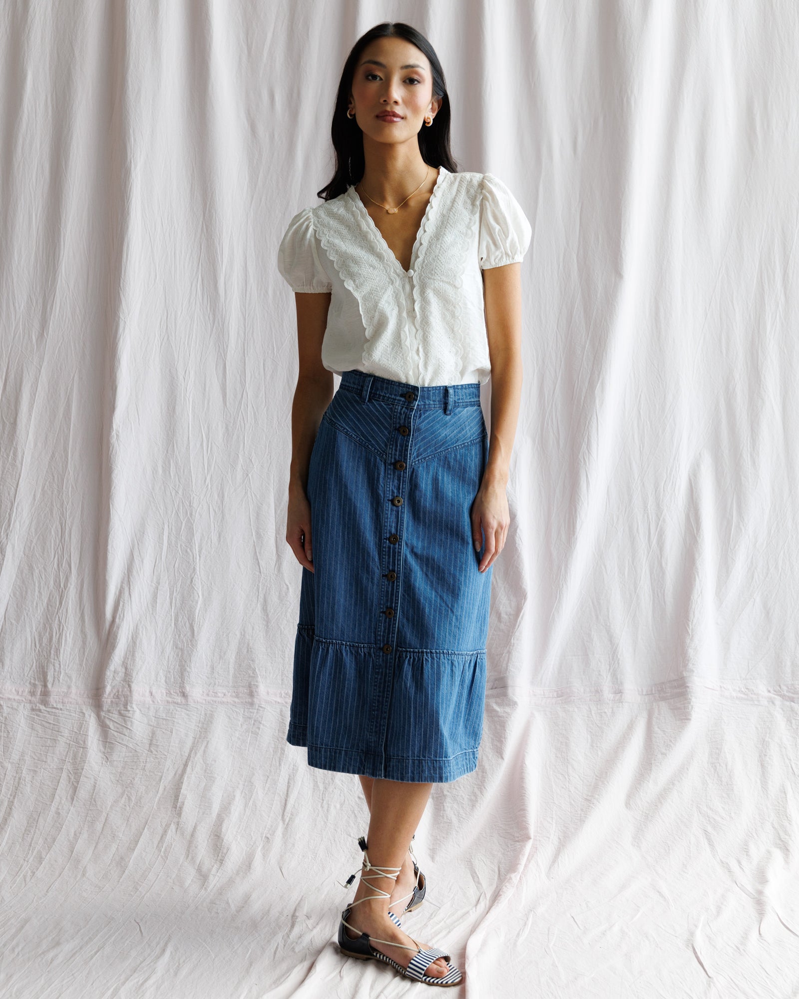 Woman wearing a white blouse and blue denim skirt against a white background