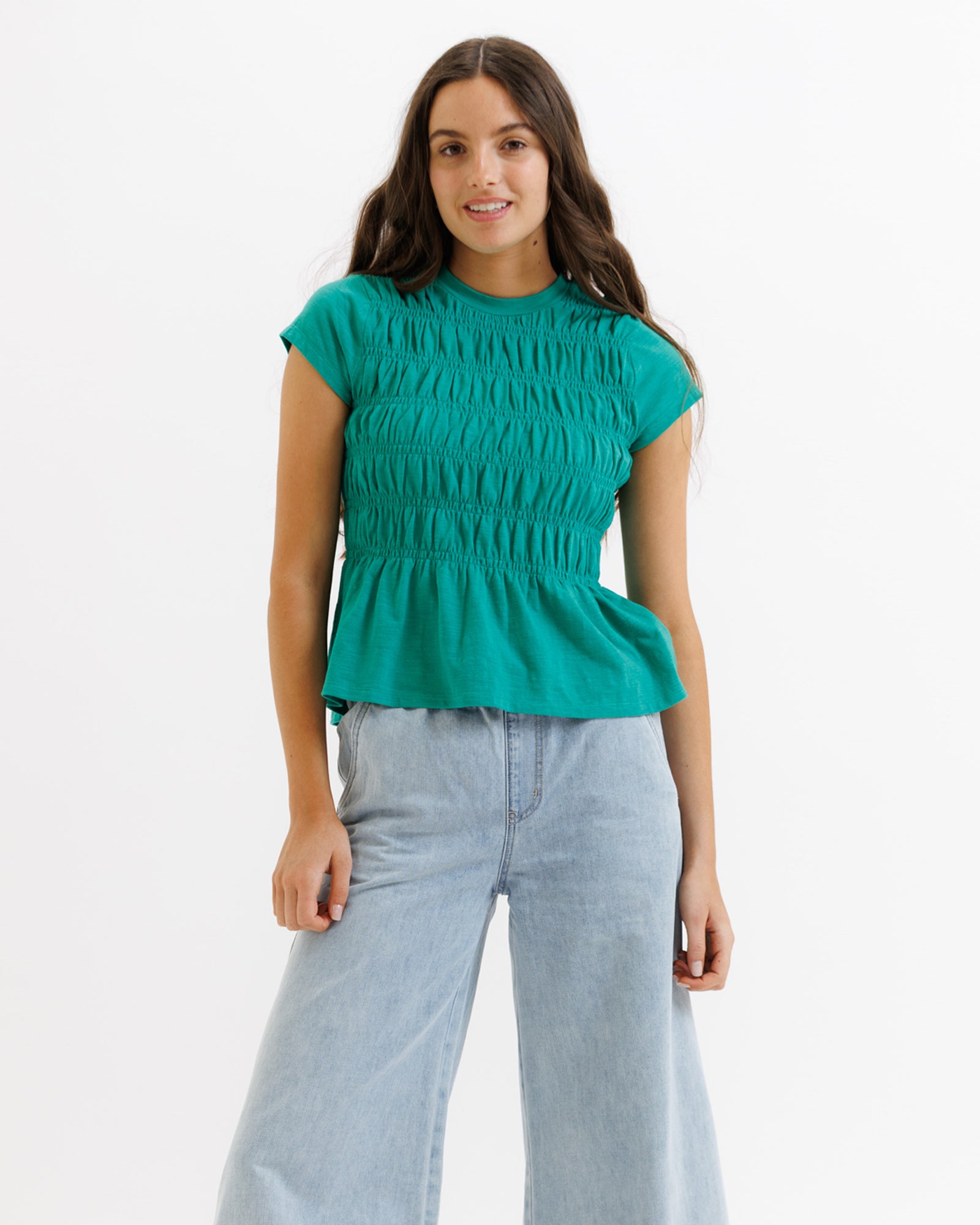 Woman wearing a teal peplum top and light blue jeans on a white background