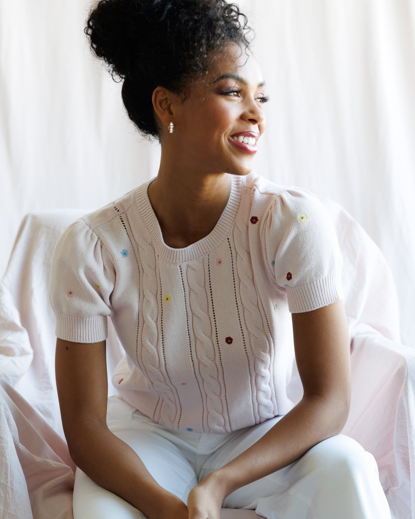 Woman wearing a white sweater with colorful buttons sitting on a white couch.