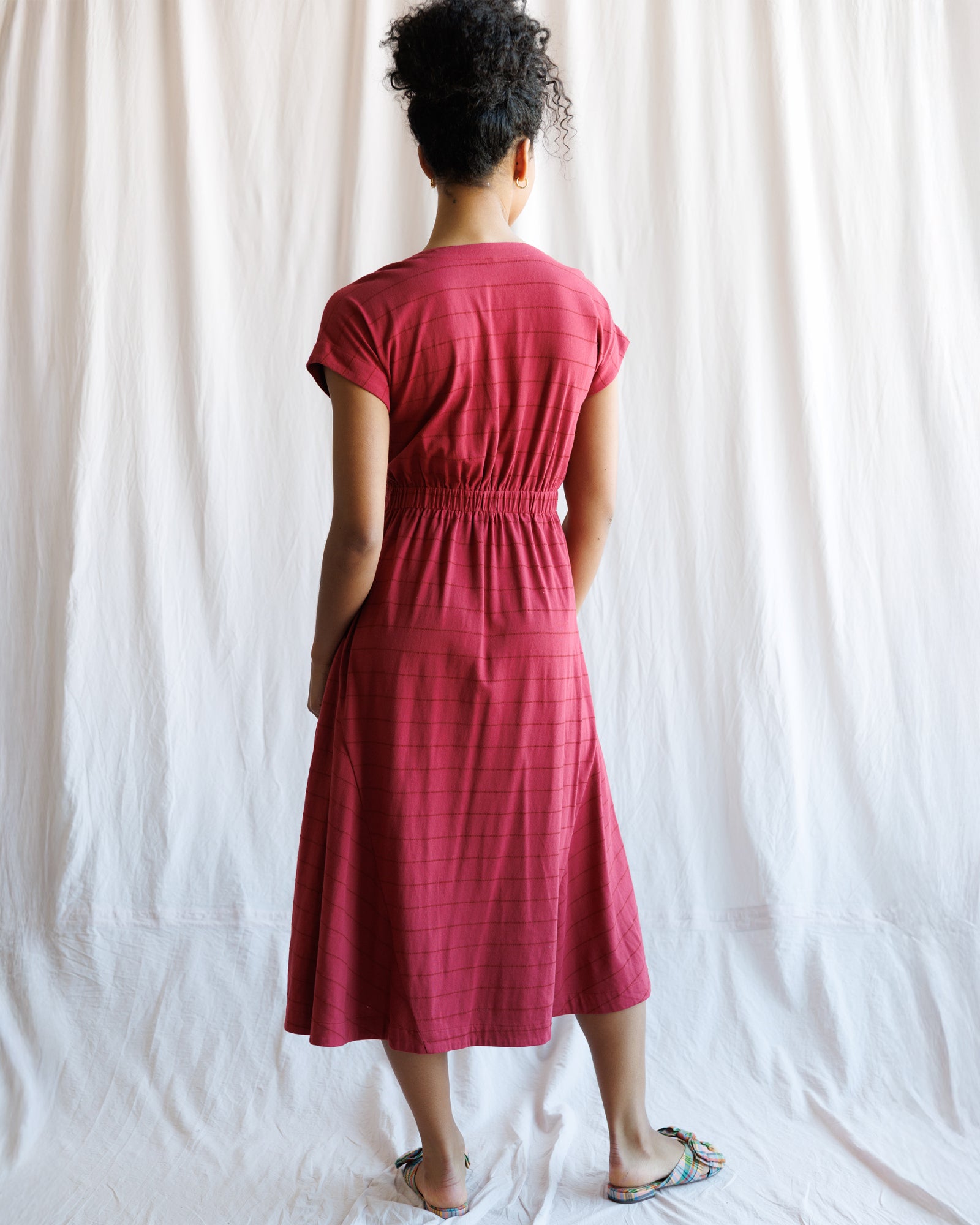 Person wearing a red dress standing against a white curtain