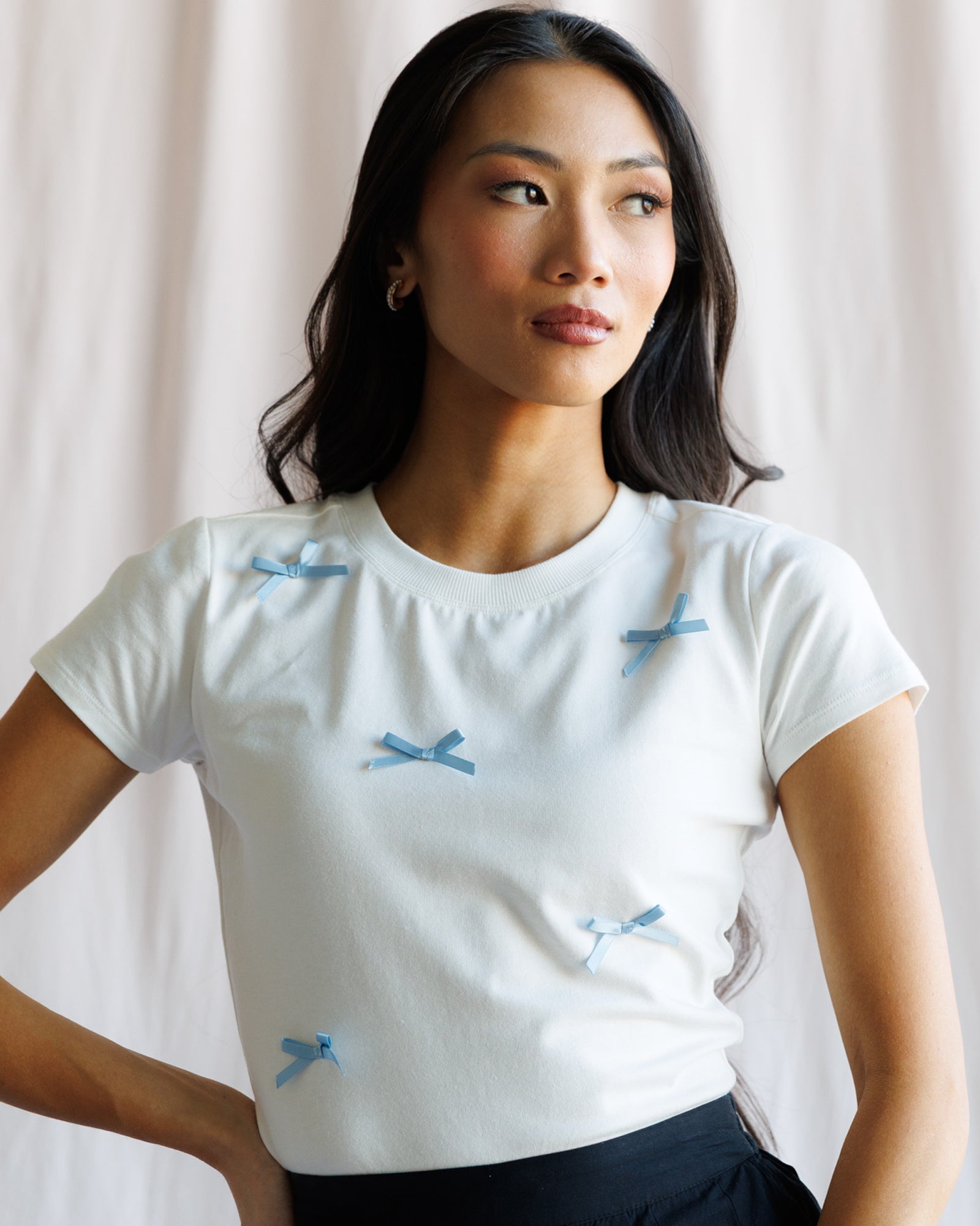 Woman wearing a white t-shirt with blue bow patterns against a plain background