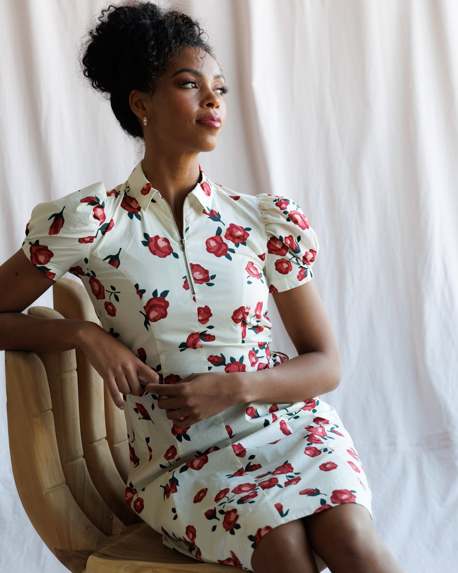 Woman wearing a floral dress sitting on a chair against a plain background