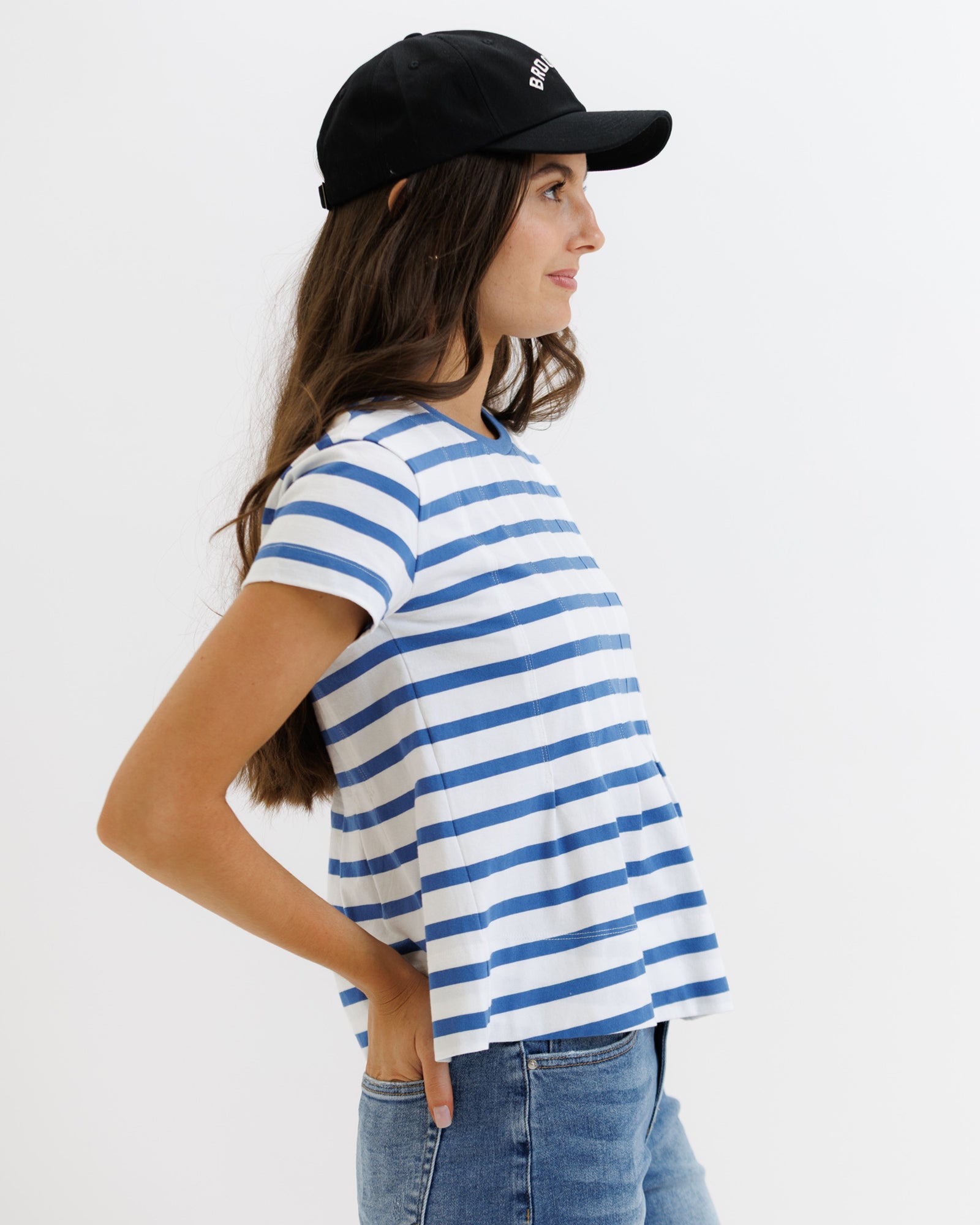 Woman wearing a blue and white striped t-shirt, black cap, and jeans on a white background