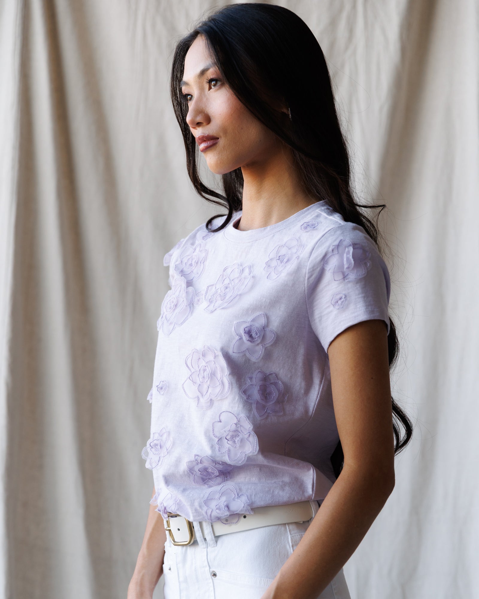 Woman wearing a white floral blouse against a beige curtain background