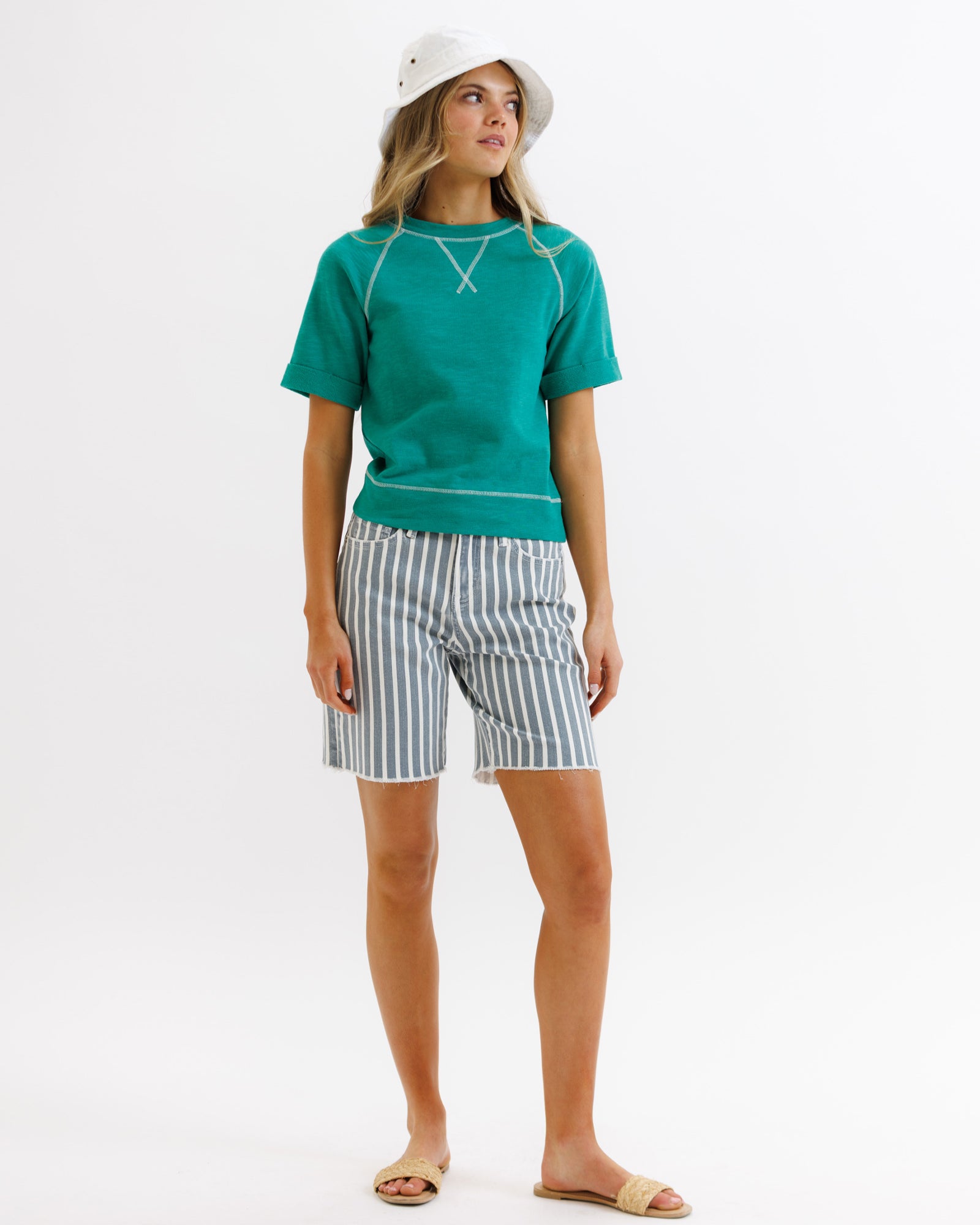 Woman wearing a green top and striped shorts on a white background
